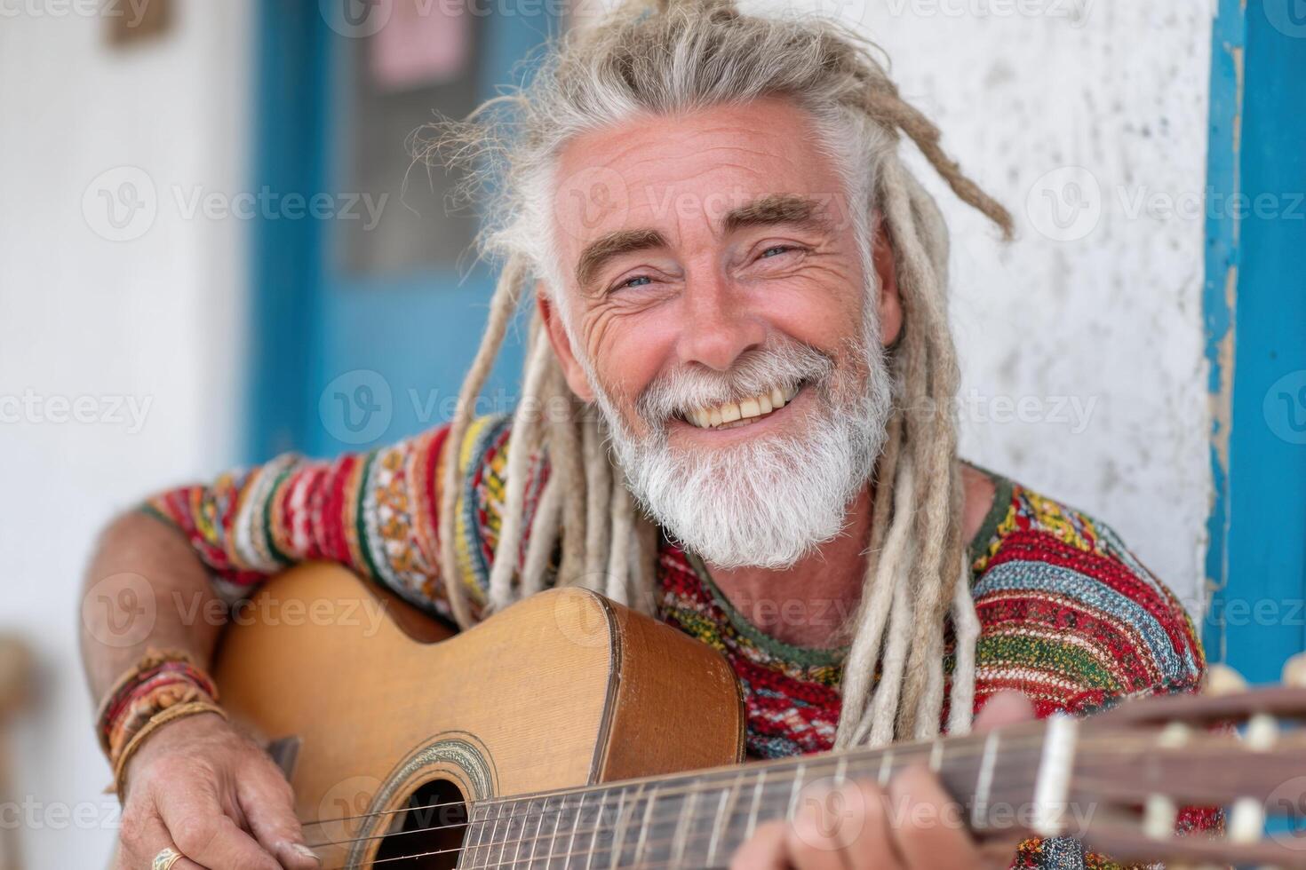 Elderly man with long dreadlocks wearing colorful sweater is playing acoustic guitar outdoors, showcasing musical talent and joyful expression in a vibrant atmosphere photo