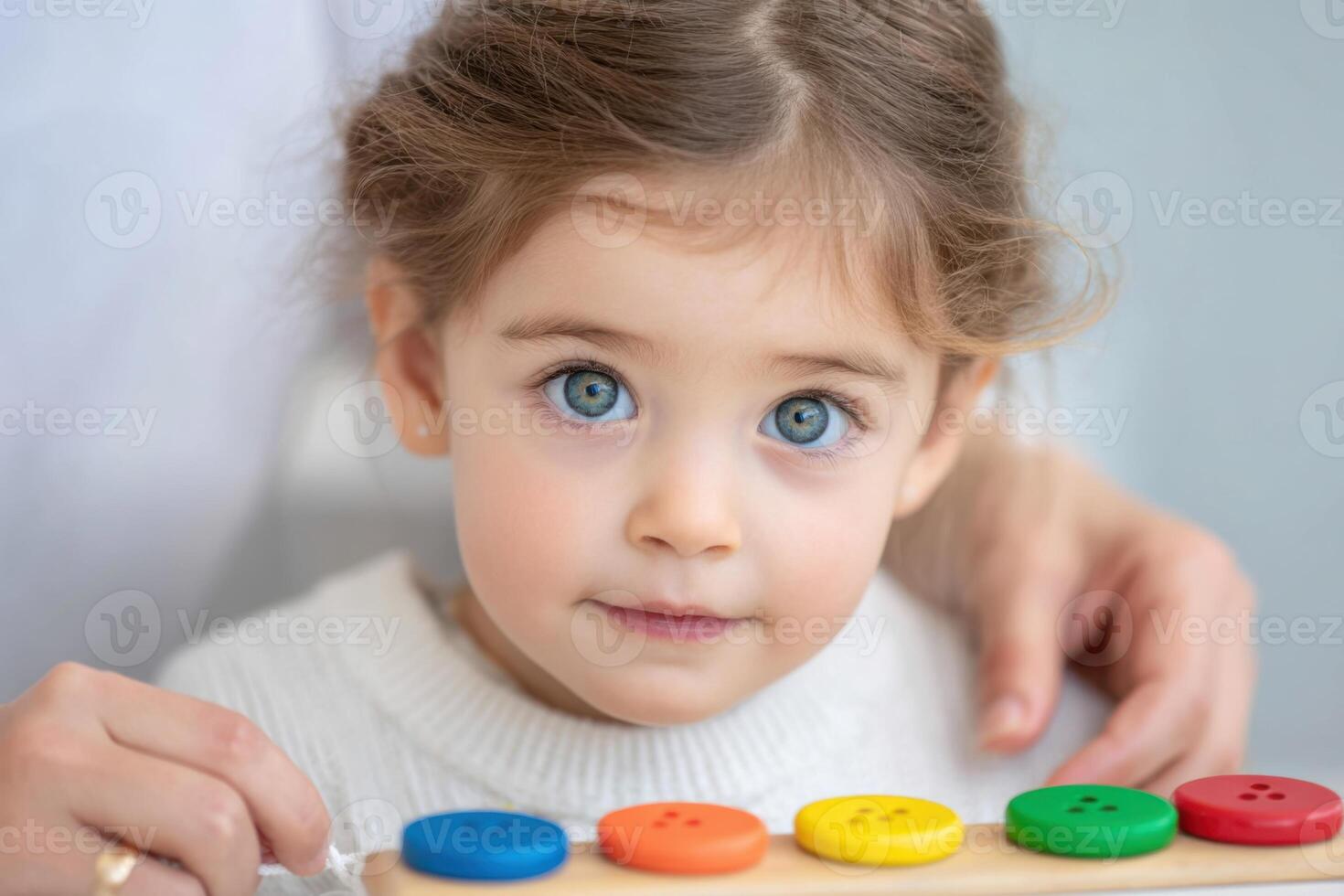 Young girl engaged in an autism occupational therapy session, focusing on colorful buttons, with a caring adult's hand guiding her, fostering development and learning through play photo