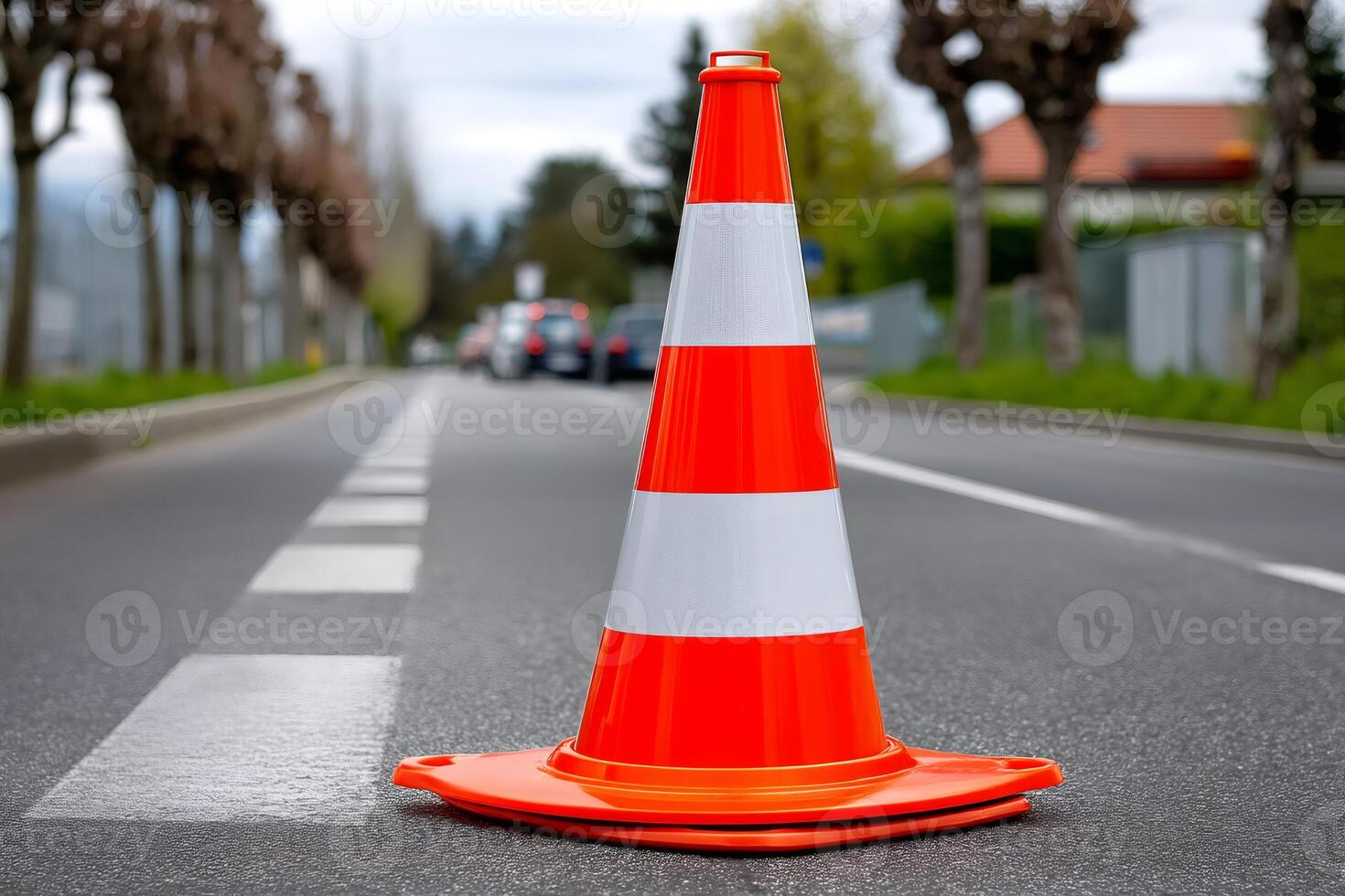 Orange and white traffic cone standing on asphalt road, cars driving in background photo
