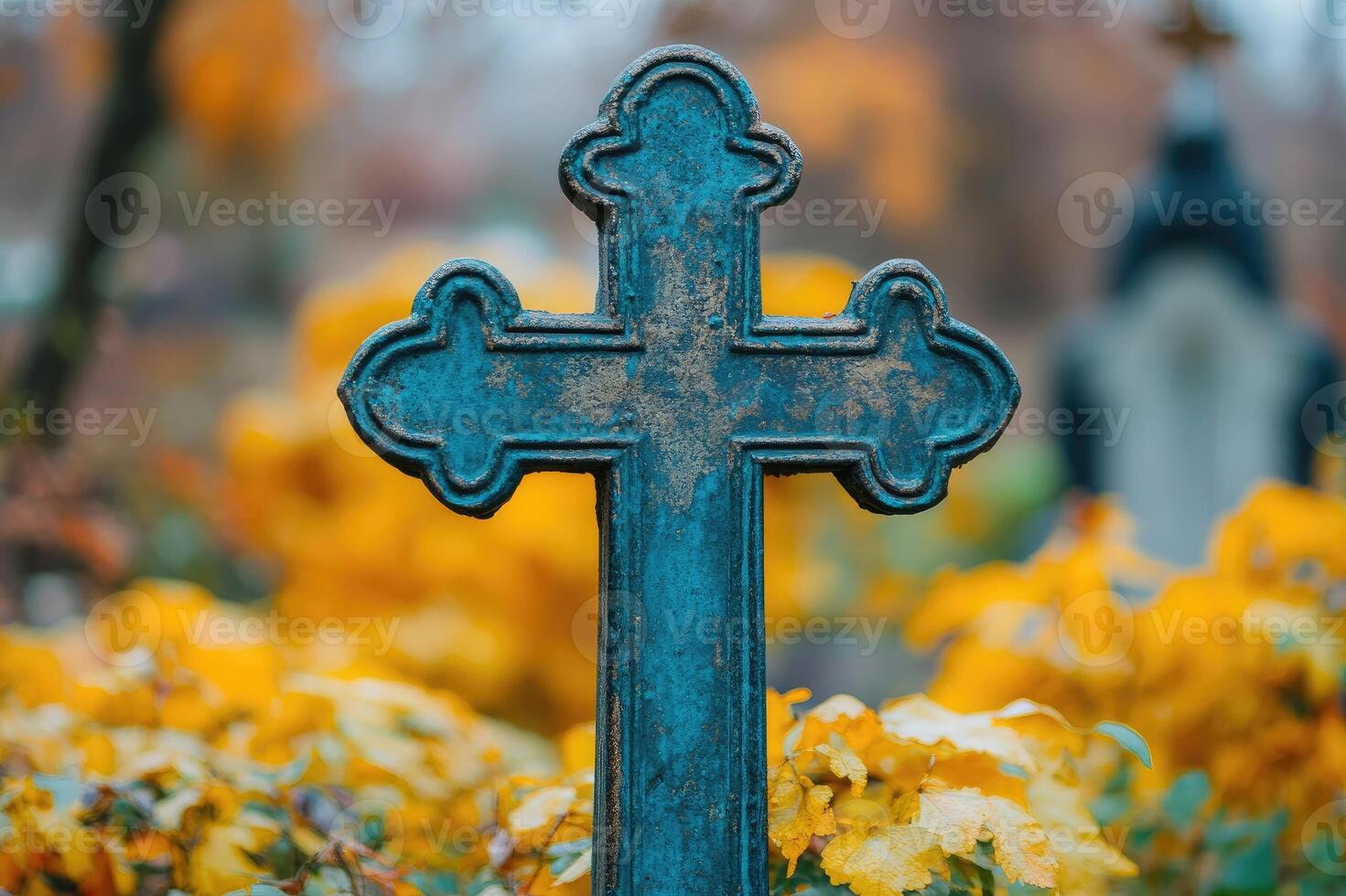 Weathered blue cross standing in cemetery with yellow flowers blooming in autumn photo