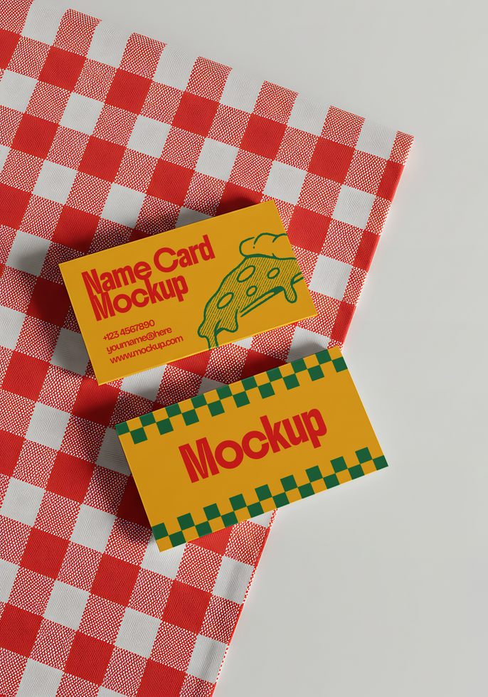 Two yellow business cards with pizza and checkered designs rest on a red and white gingham tablecloth psd