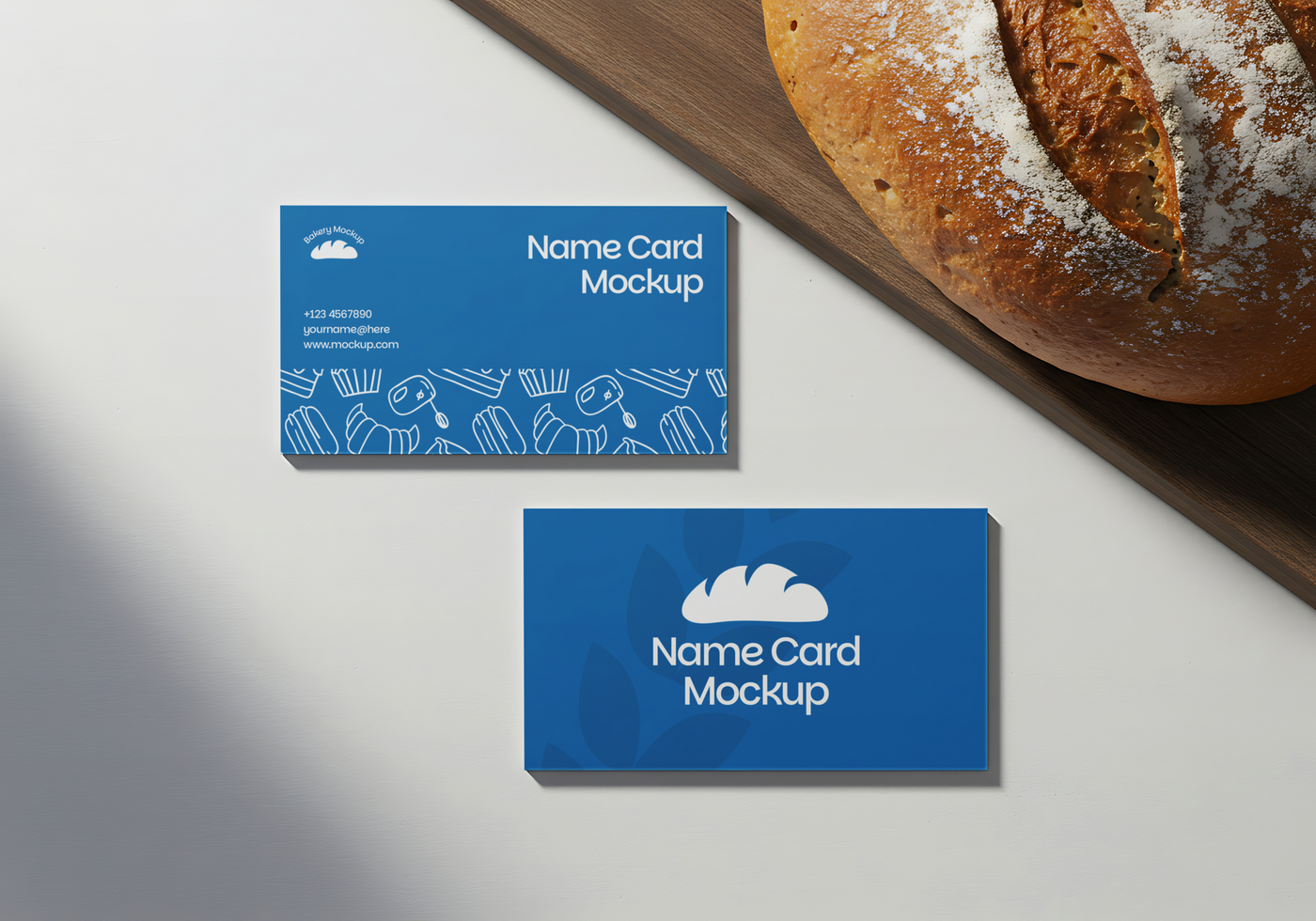 Blue name card mockups showcasing bakery themed designs next to a freshly baked loaf of bread psd