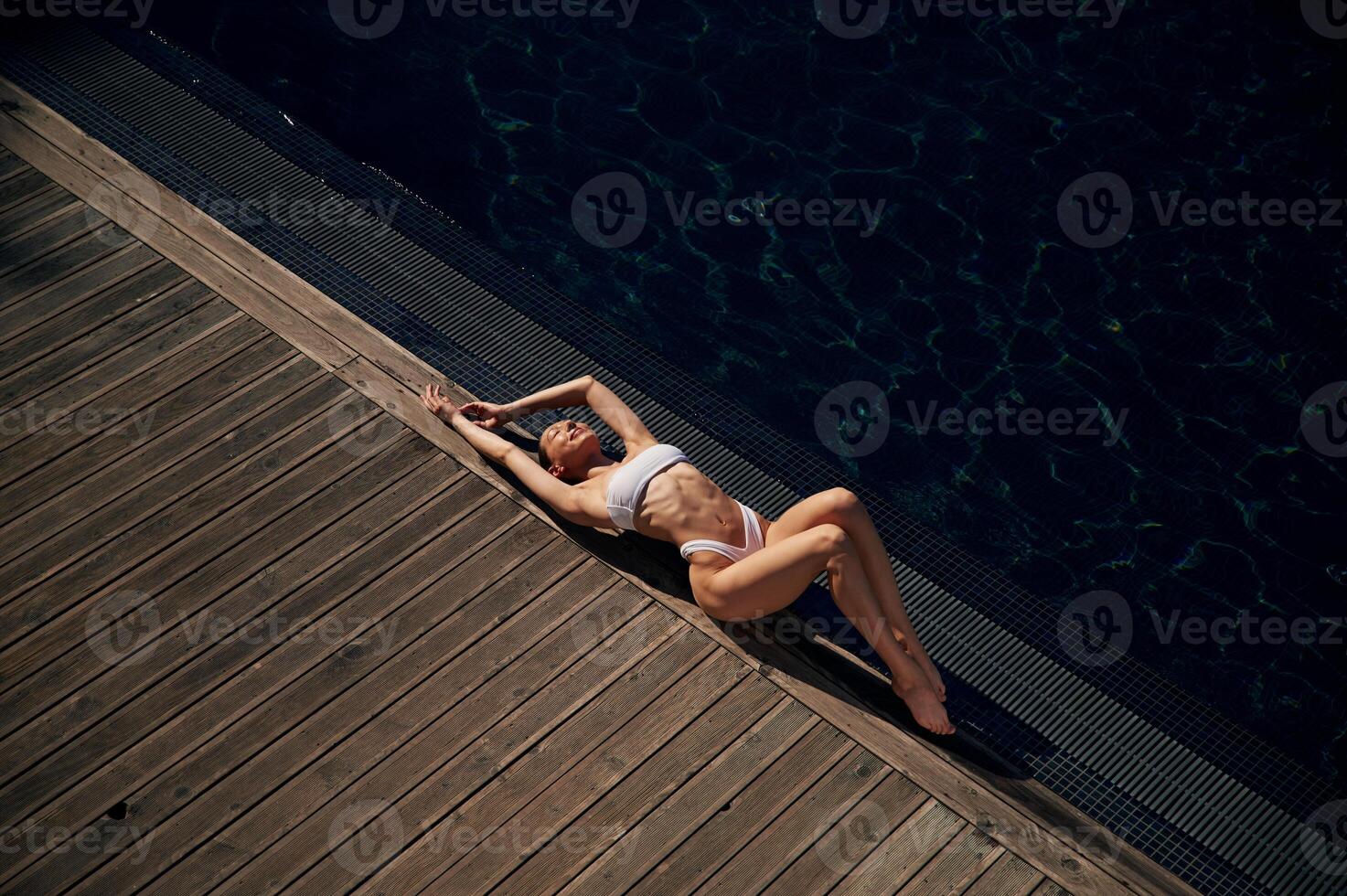 Lying down, enjoying,,, sunlight. Woman in white bikini is near swimming pool photo