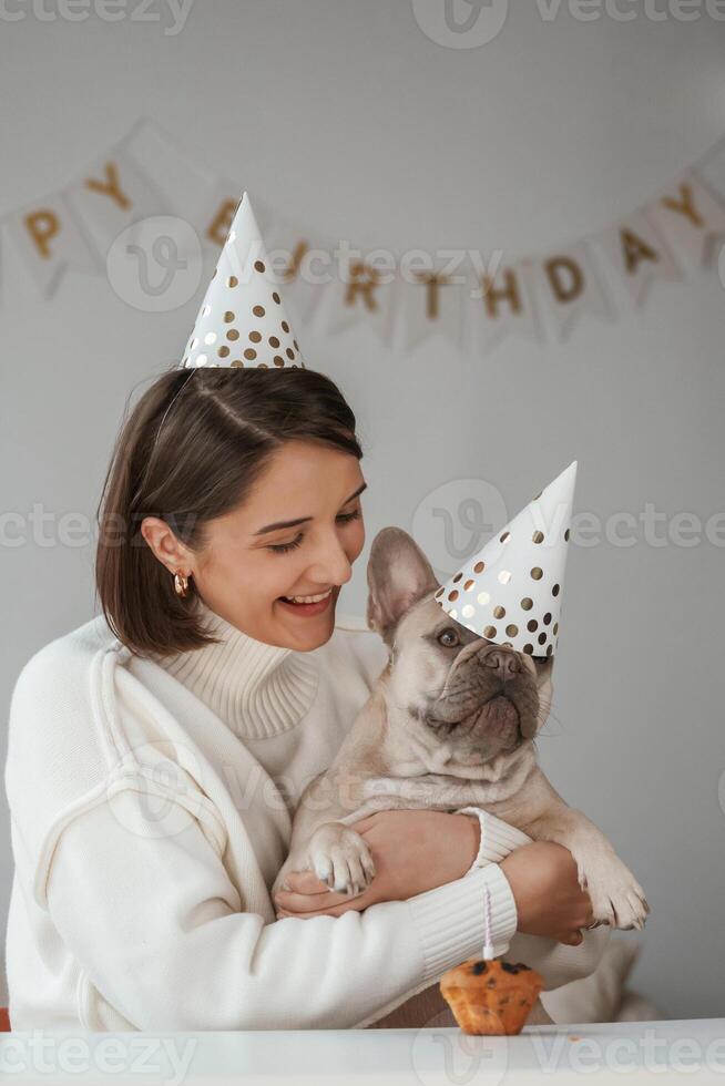 Celebration of birthday. In hats and with cake. Young woman is with her pug dog at,, home photo