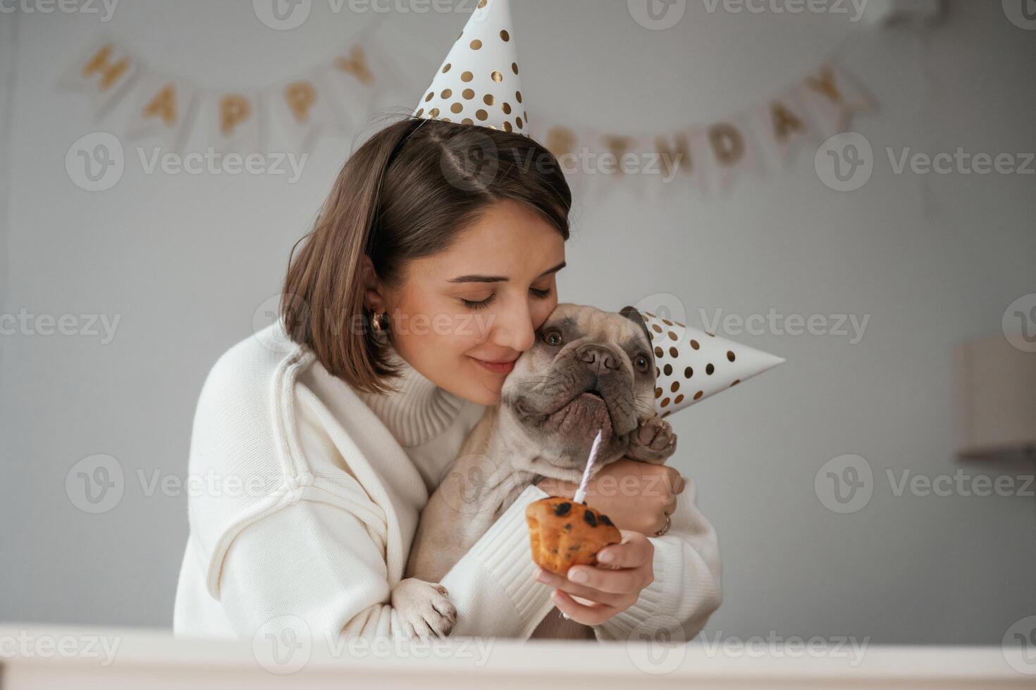 Happy, owner is, celebrating birthday of pet. In hat and with cake. Young woman is with her pug dog at home photo