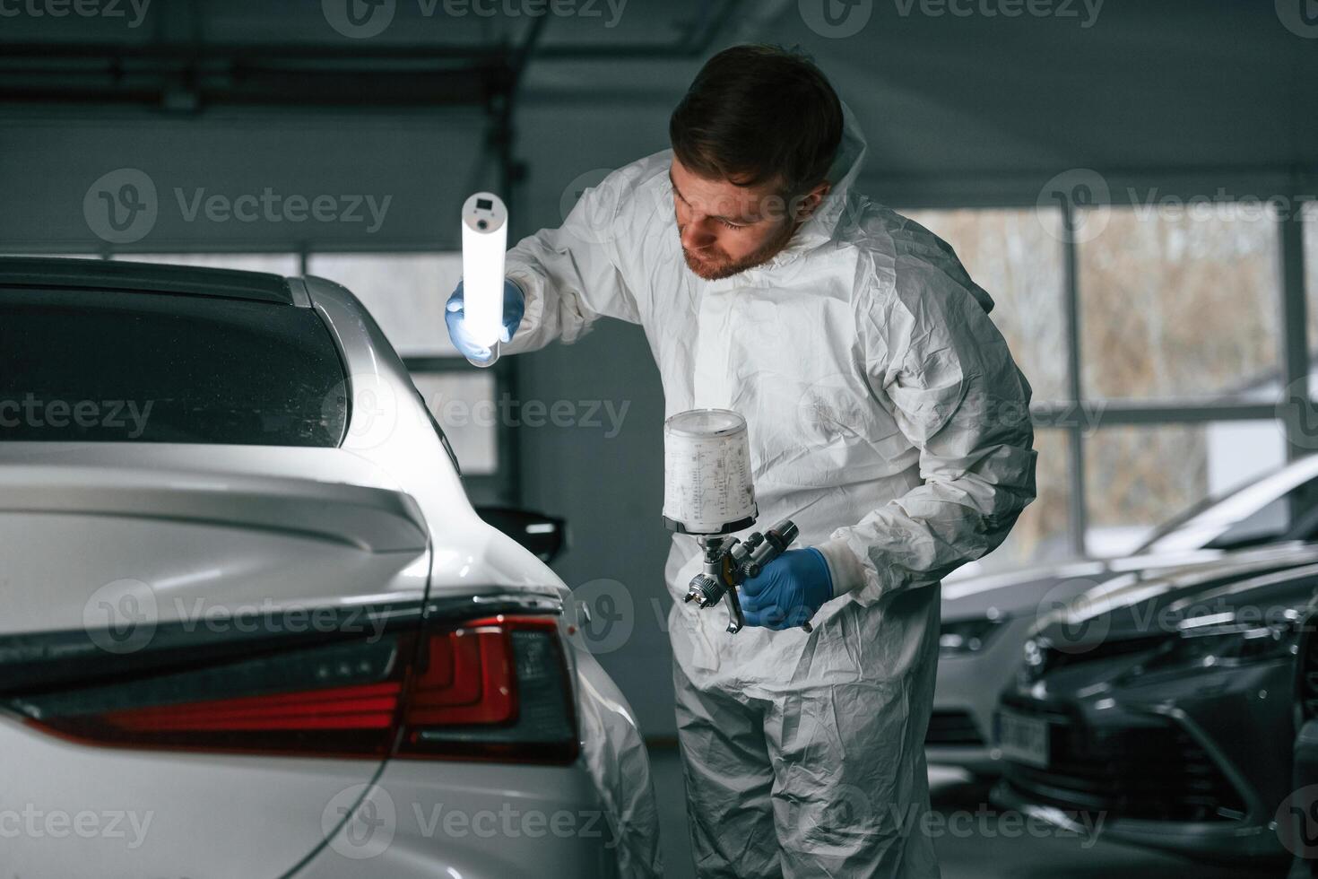 Rear,, part of automobile. Garage worker is holding lighting and checking surface of the car photo