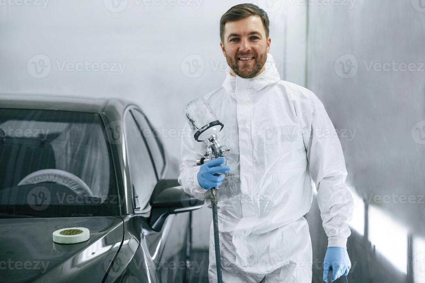 Bright, artificial lighting. Man is standing and holding spray gun with paint for automobile photo