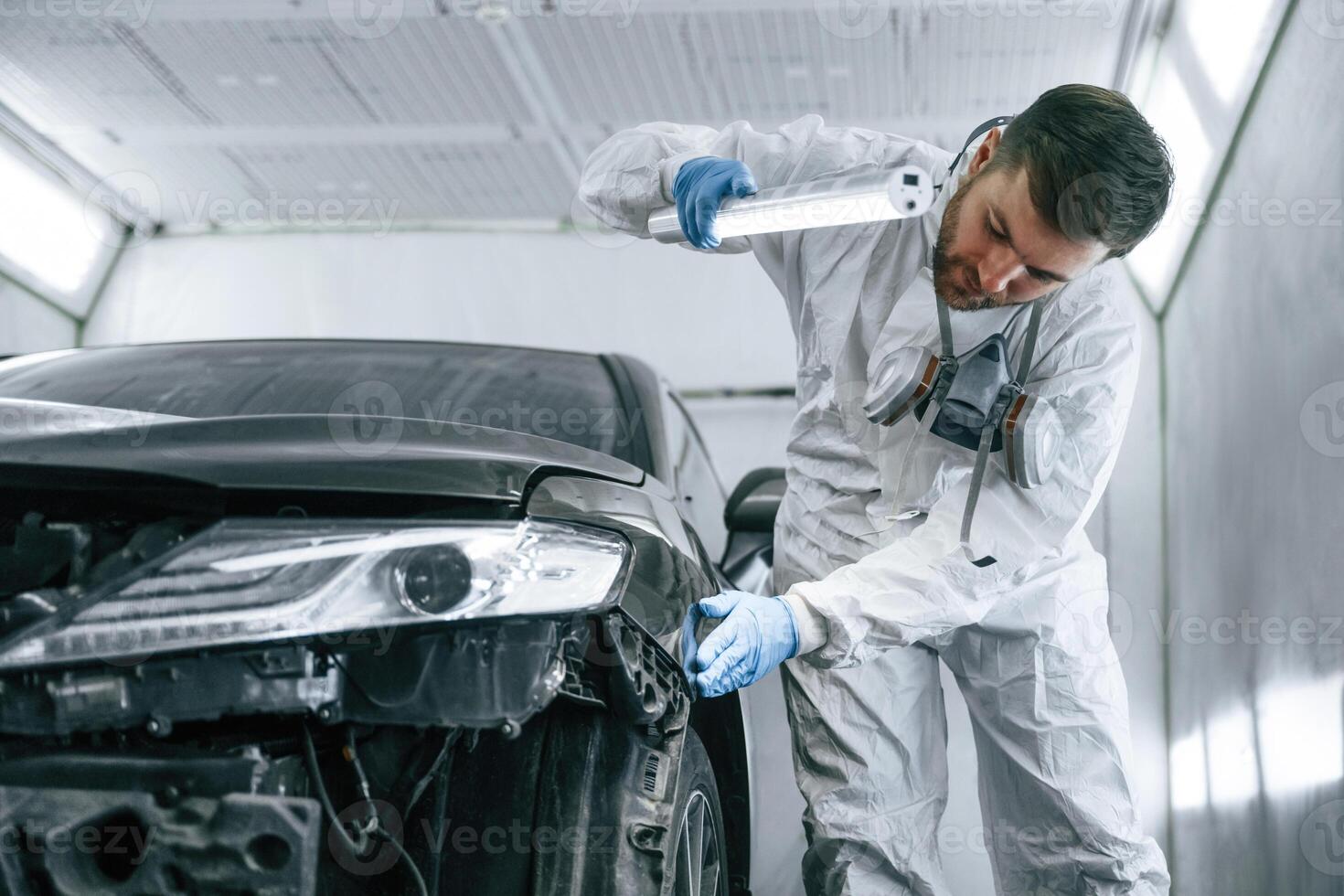Front view. Garage worker ,is,, holding lighting and checking surface of the car photo