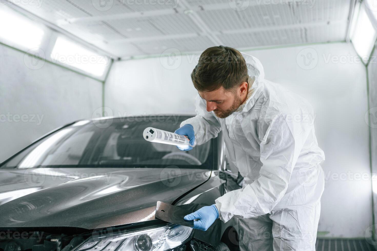 Choosing right color. Garage,, worker, is holding lighting and checking surface of the car photo