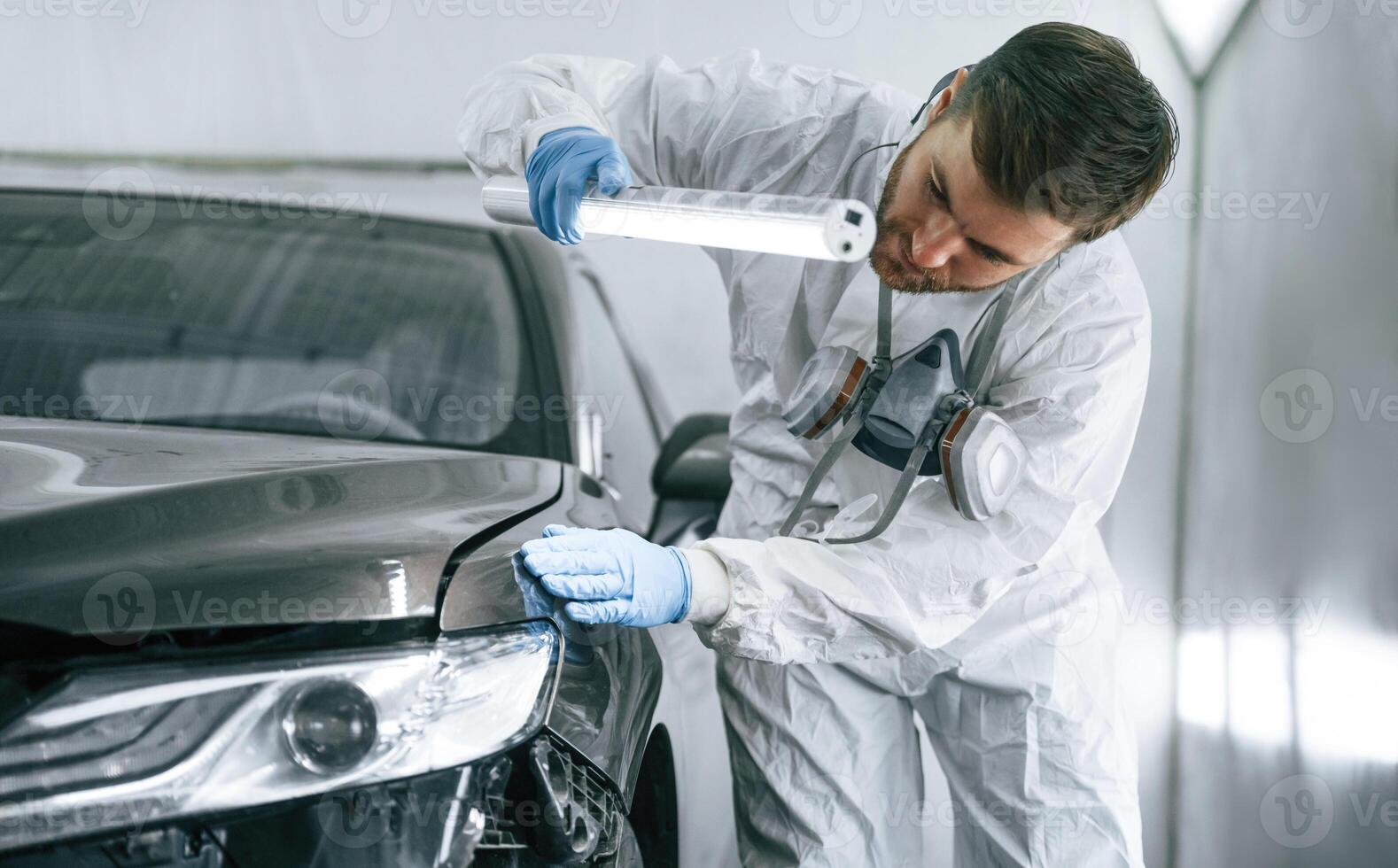 Front view. Garage worker, is ,holding lighting and checking surface of the car photo