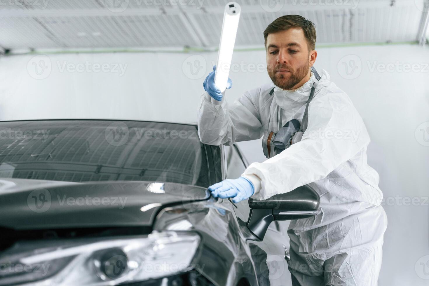 Front, view. Garage worker, is holding lighting and checking surface of the car photo