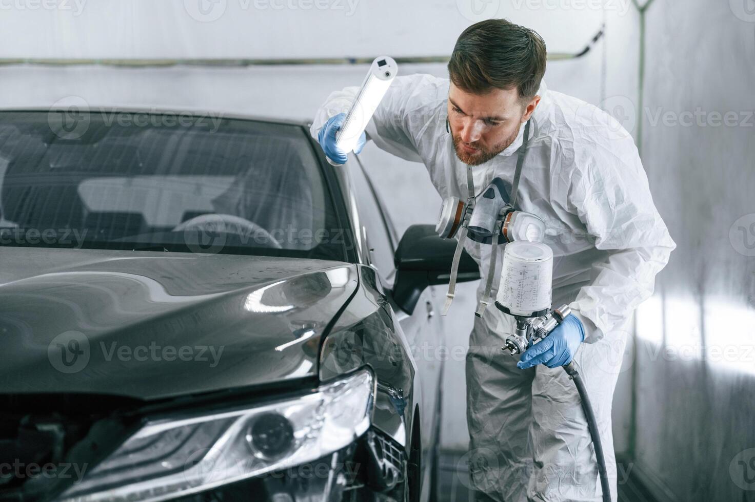 By help of lighting equipment. Man, is, painting a car by using spray guy photo