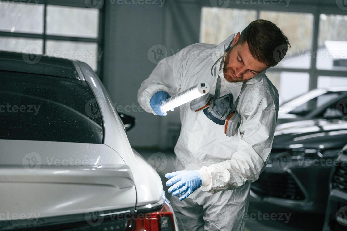 Rear part of automobile,. Garage worker is holding lighting and checking surface of the car photo