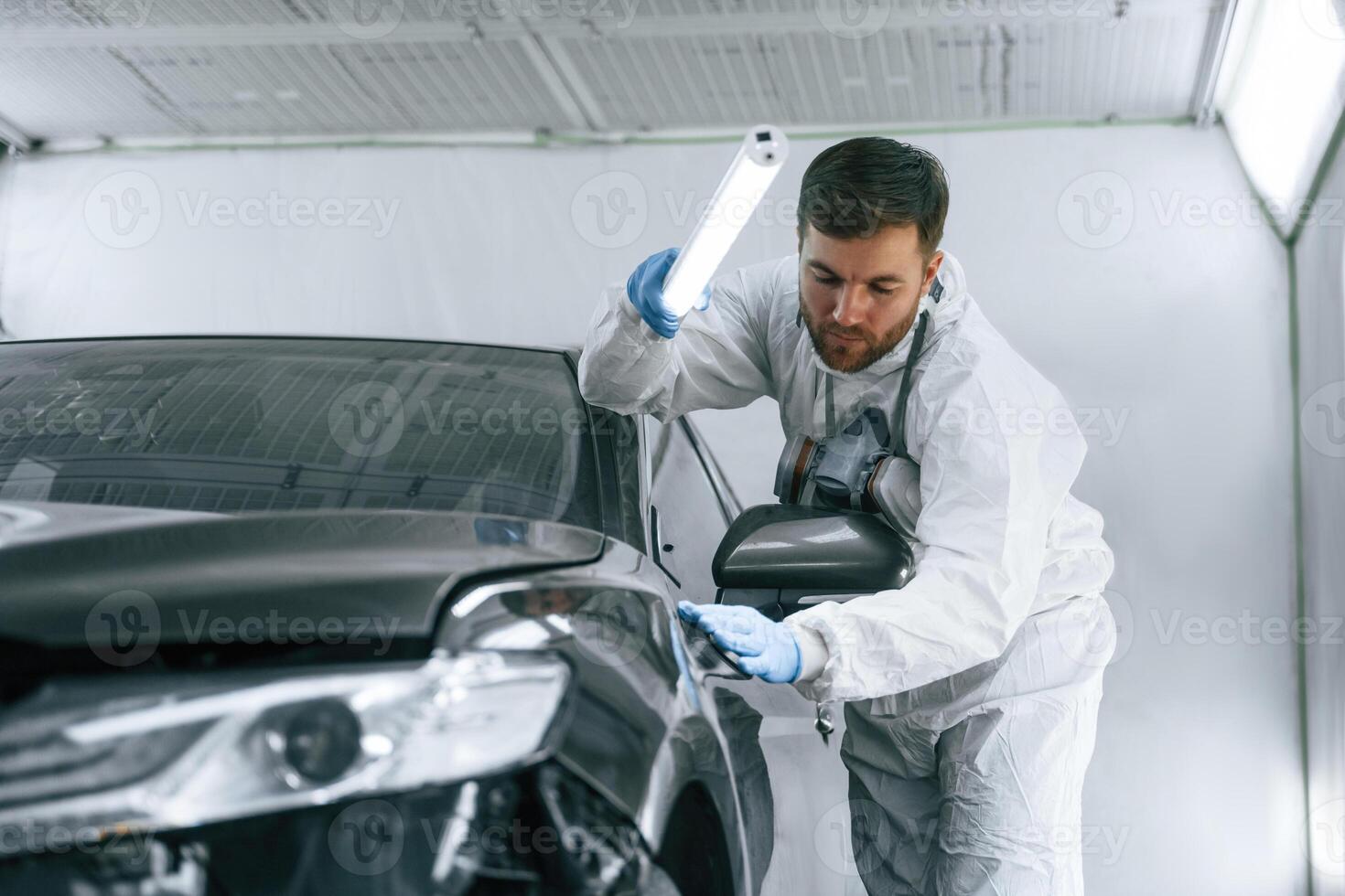 Front view... Garage worker is holding lighting and checking surface of the car photo
