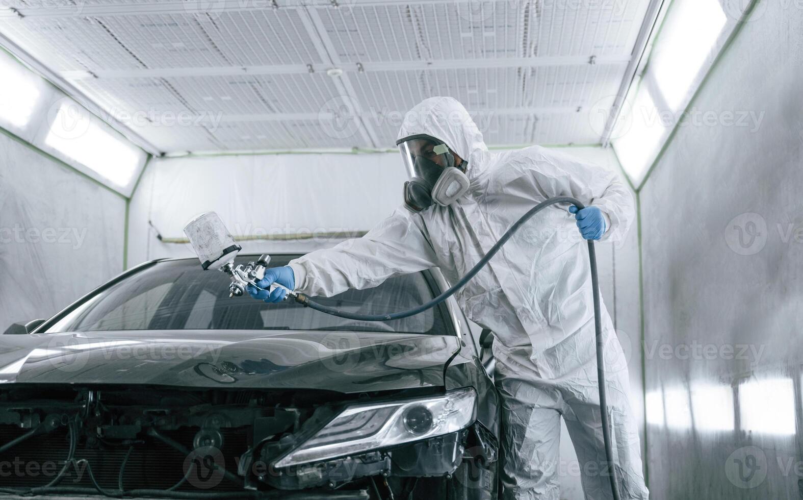 White protective wear. Man is painting, a car by using spray guy photo