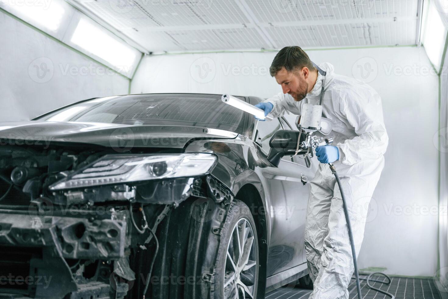 Professional worker. Man is ,,painting a car by using spray guy photo