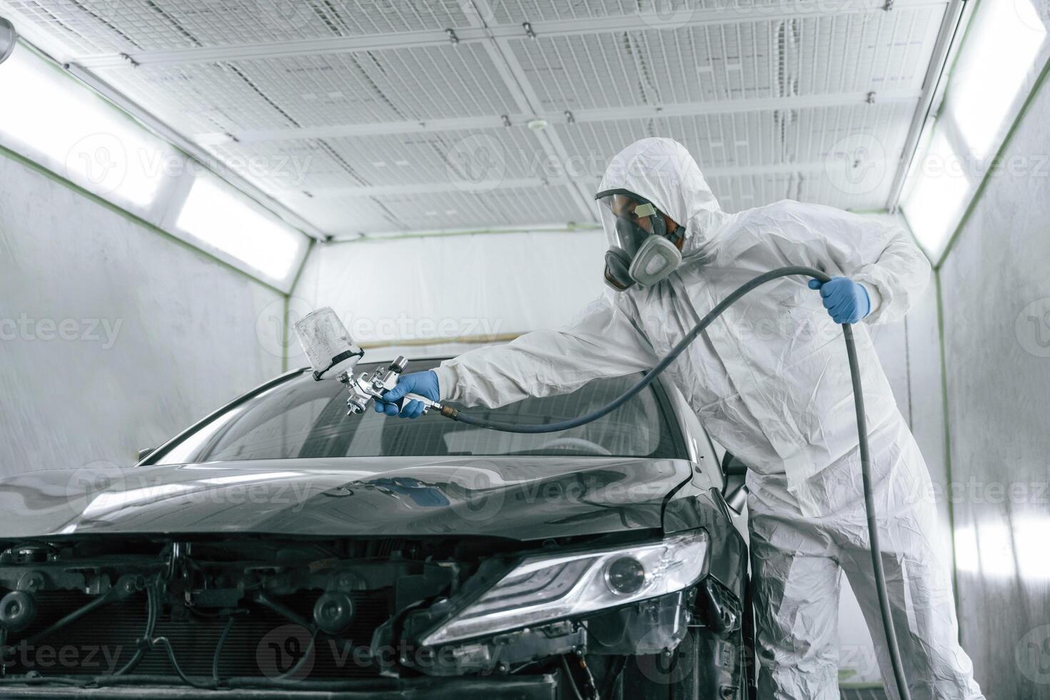 White protective wear. Man is painting a, car by using spray guy photo