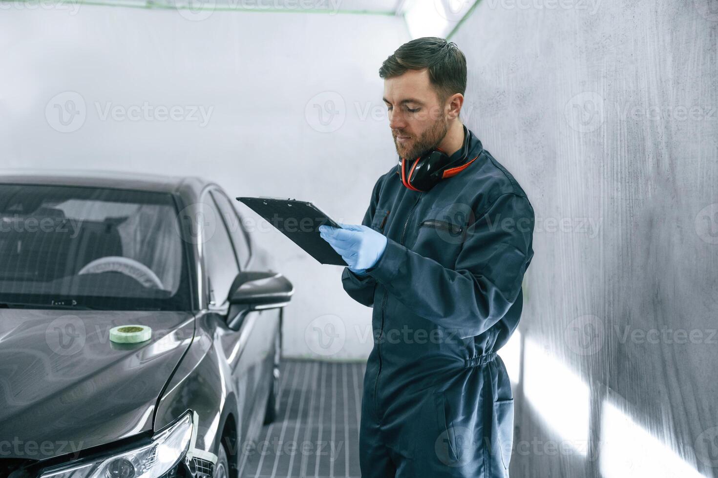 Reading information. Car painter is, standing in the garage with documents in hands photo