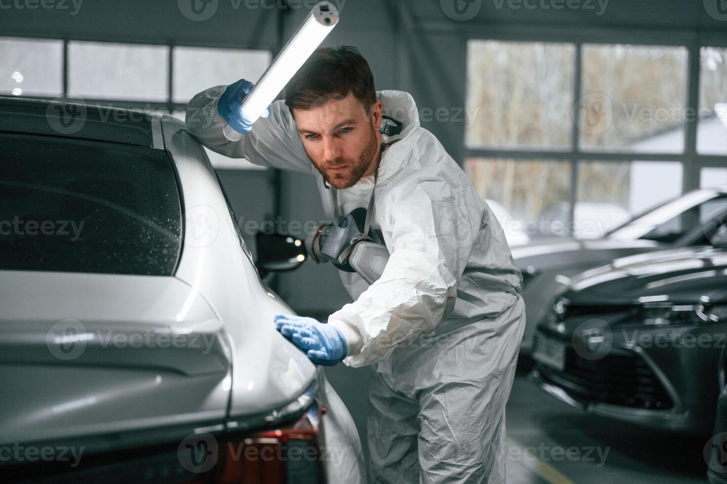 Rear part of automobile. Garage ,,worker is holding lighting and checking surface of the car photo
