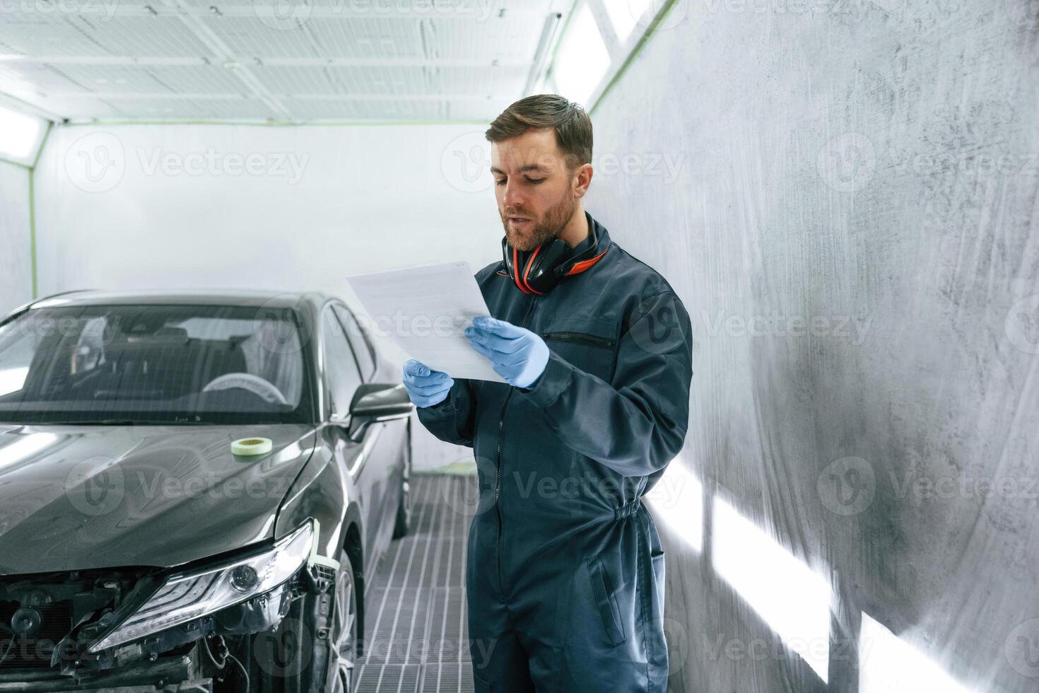 Reading information. Car painter ,is standing in the garage with documents in hands photo