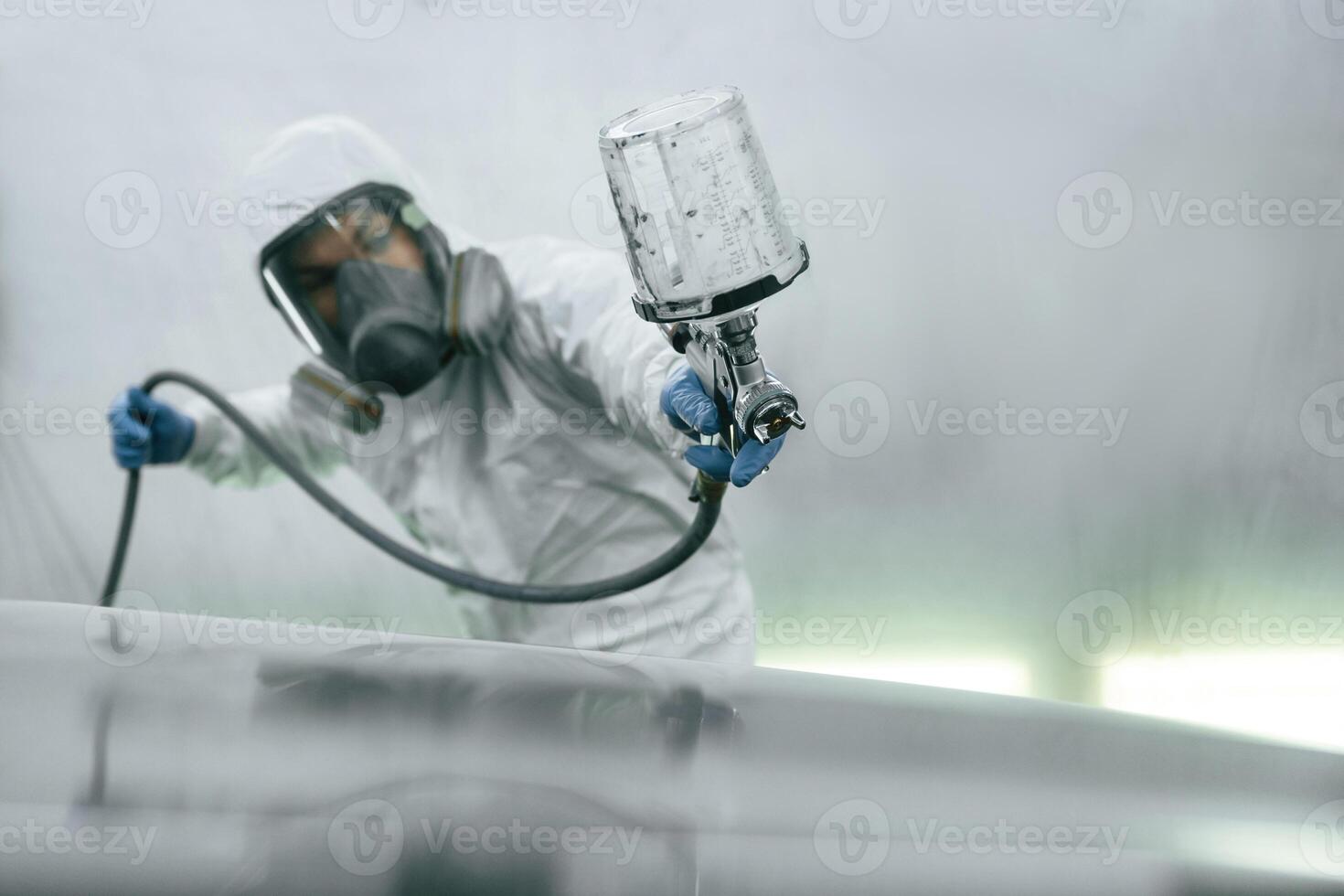 In protective mask and ,,wear. Close up view of man that is painting a car by using spray guy photo