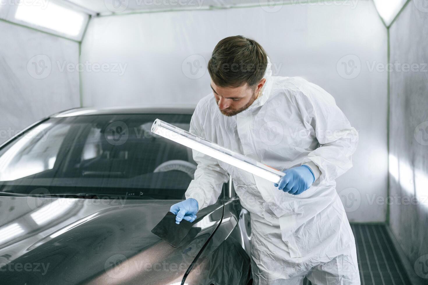 Front part, of, the automobile. Garage worker is holding lighting and checking surface of the car photo