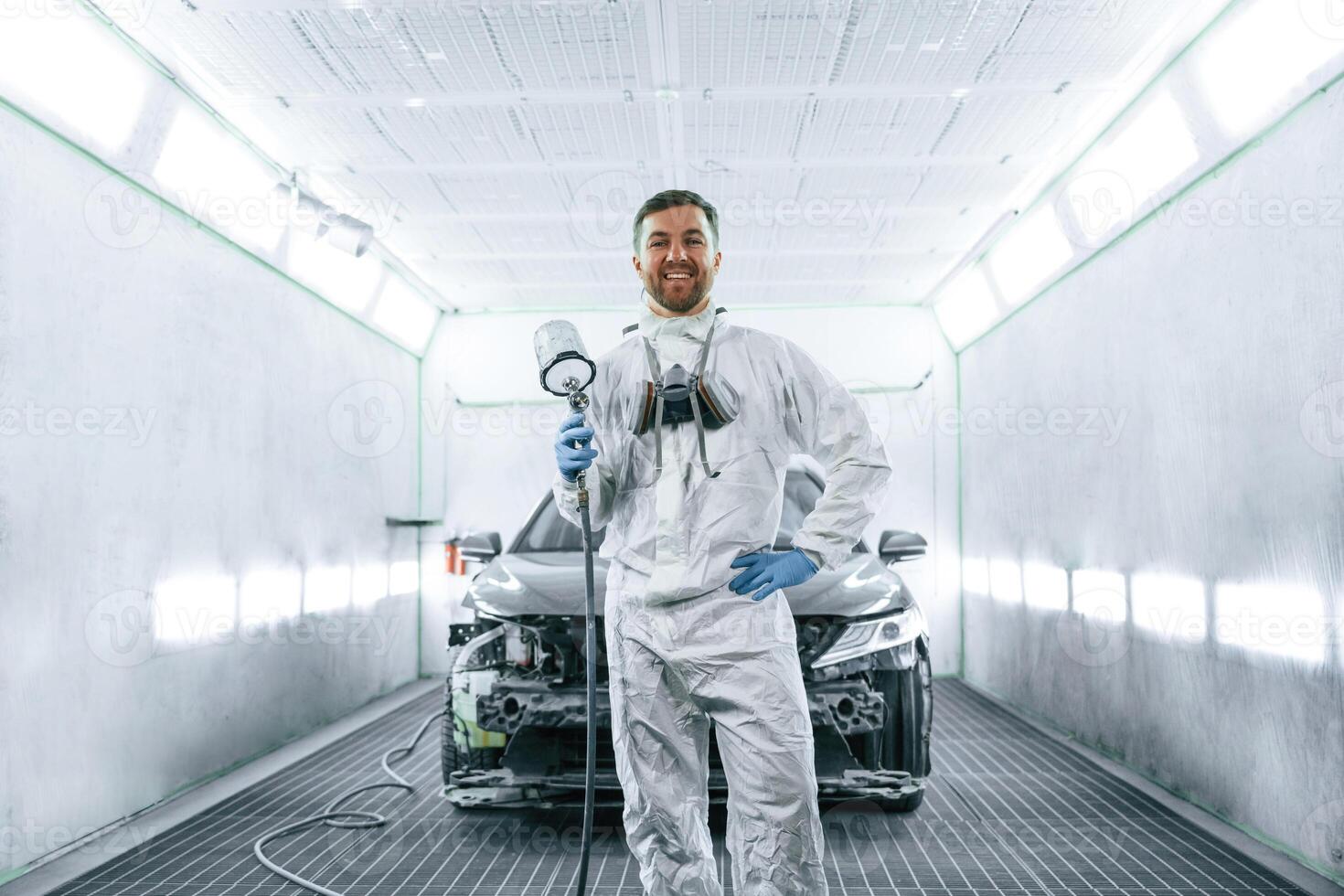Bright artificial ,lighting. Man is standing and holding spray gun with paint for automobile photo