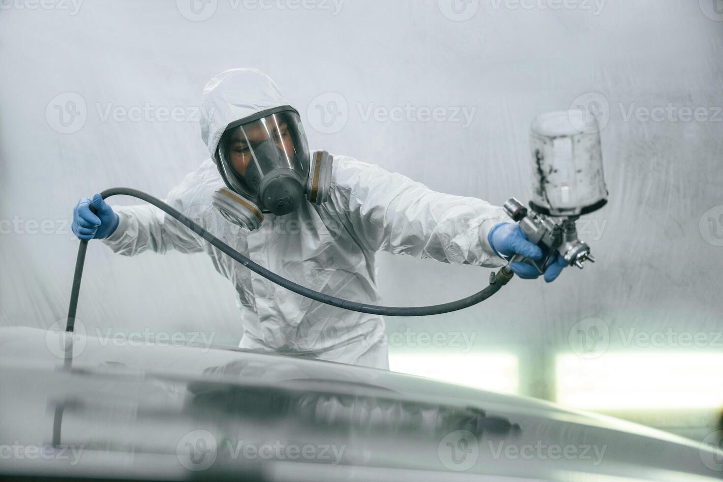 In, protective mask and wear. Close up view of man that is painting a car by using spray guy photo