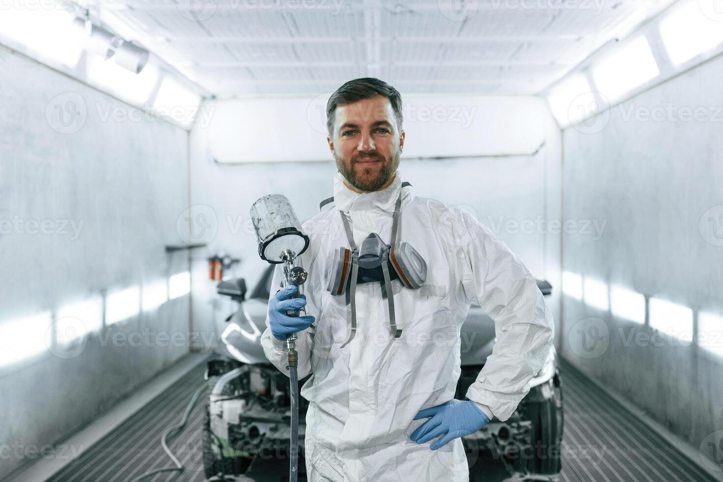 Brigh,t artificial lighting. Man is standing and holding spray gun with paint for automobile photo