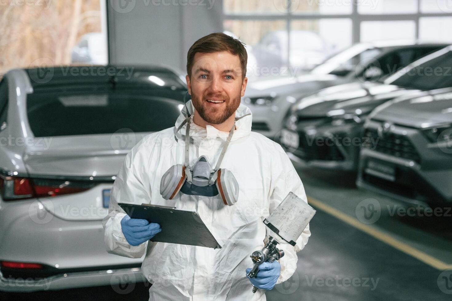 Positive facial expression.,, Car painter is standing in the garage with documents in hands photo