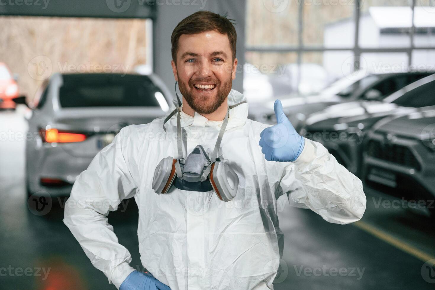 Standing, in ,the garage with cars. Portrait of professional painter with mask photo