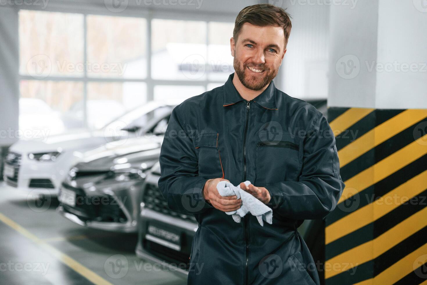 Wiping ,hands. Repairman in, uniform is standing in the garage with cars photo