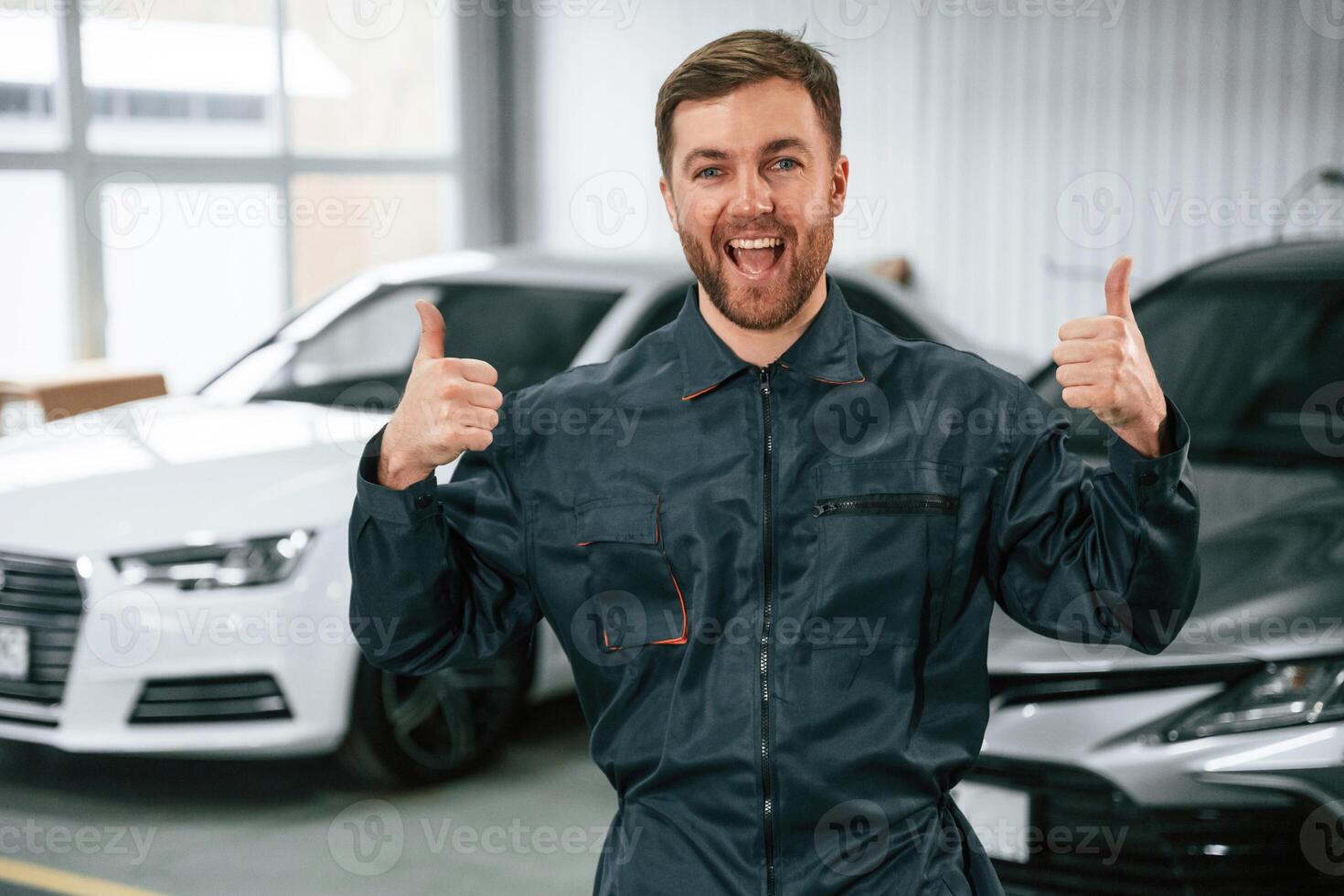 Handsome friendly guy. Repairman,, in uniform is standing in the garage with cars photo