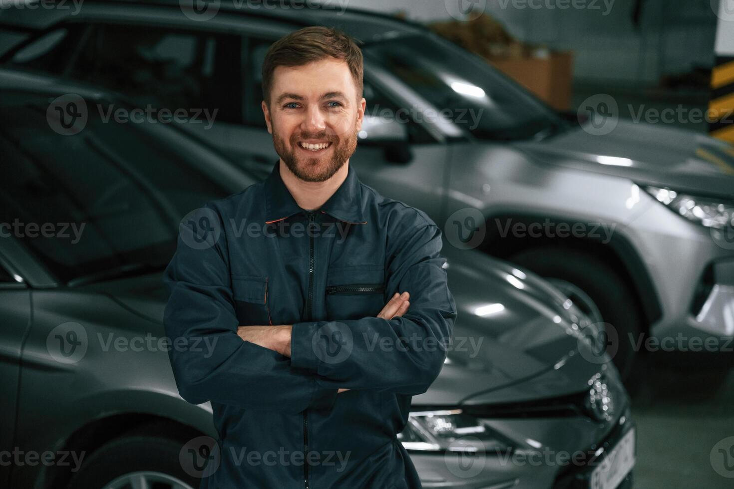 Repairman ,in ,,uniform is standing in the garage with cars photo