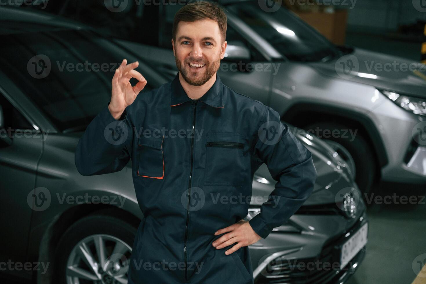 Repairman in, uniform, is standing in the garage with cars photo