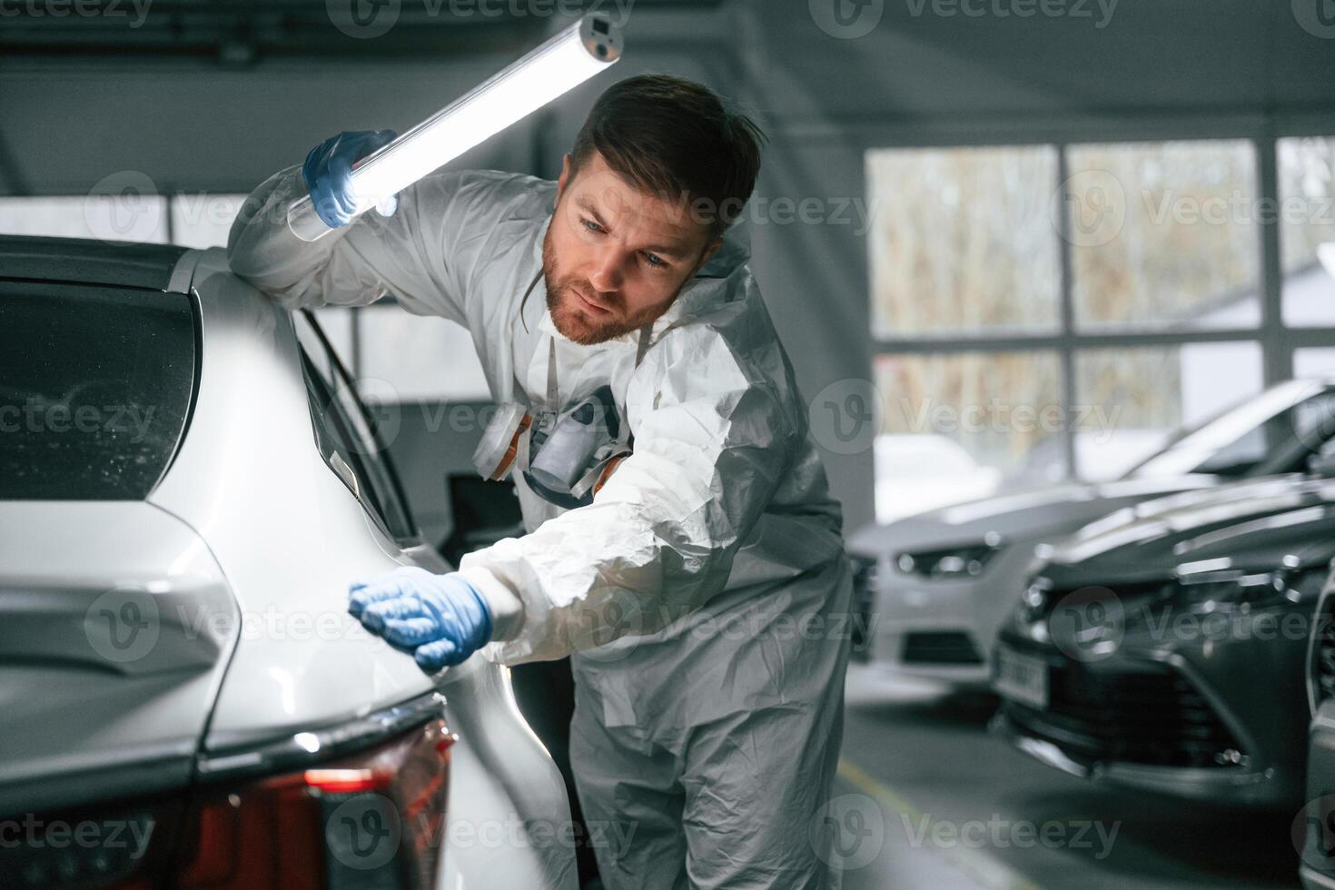 Searching for, imperfections.. Garage worker is holding lighting and checking surface of the car photo
