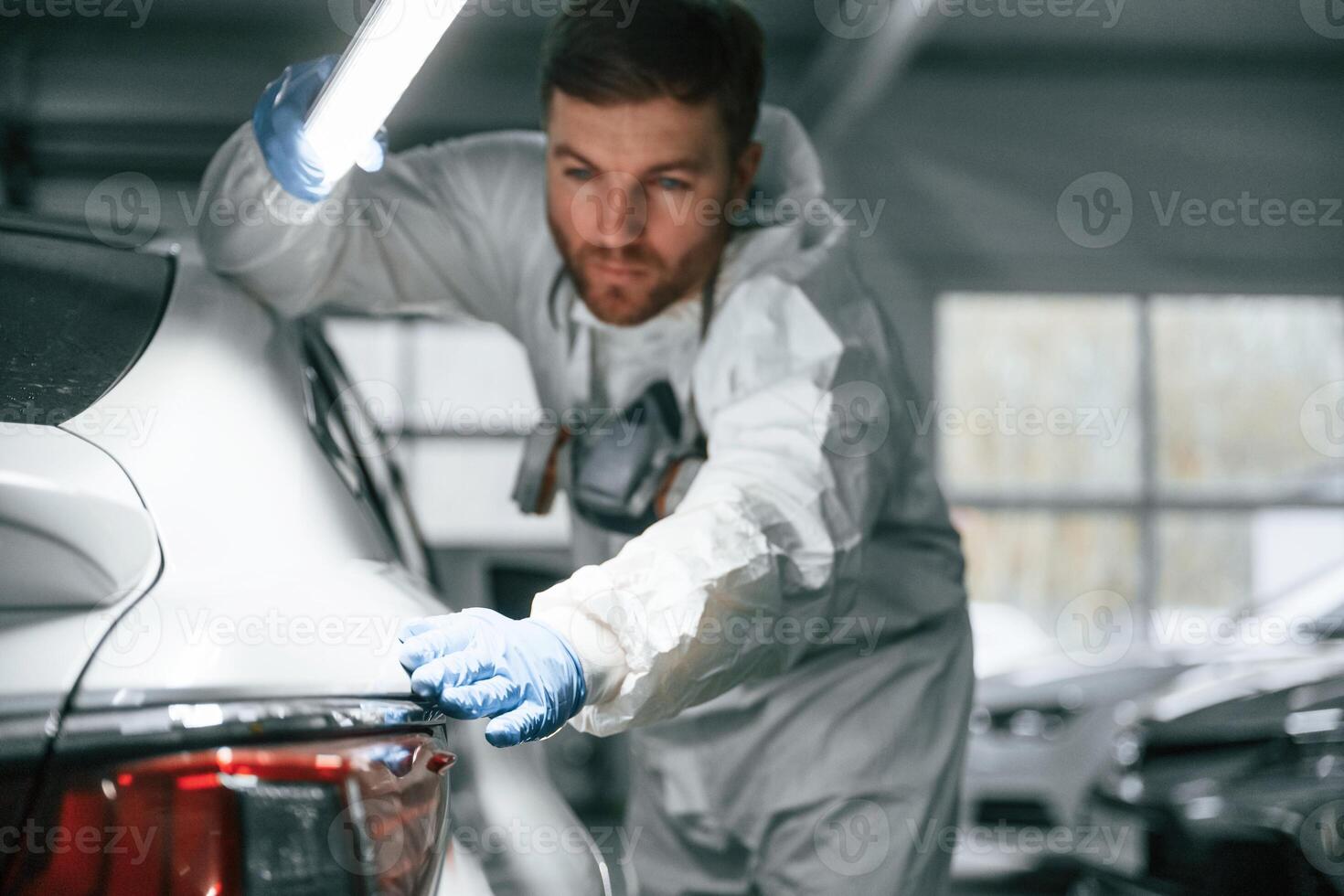 Searching for, imperfections. Garage worker is holding lighting and checking surface of the car photo