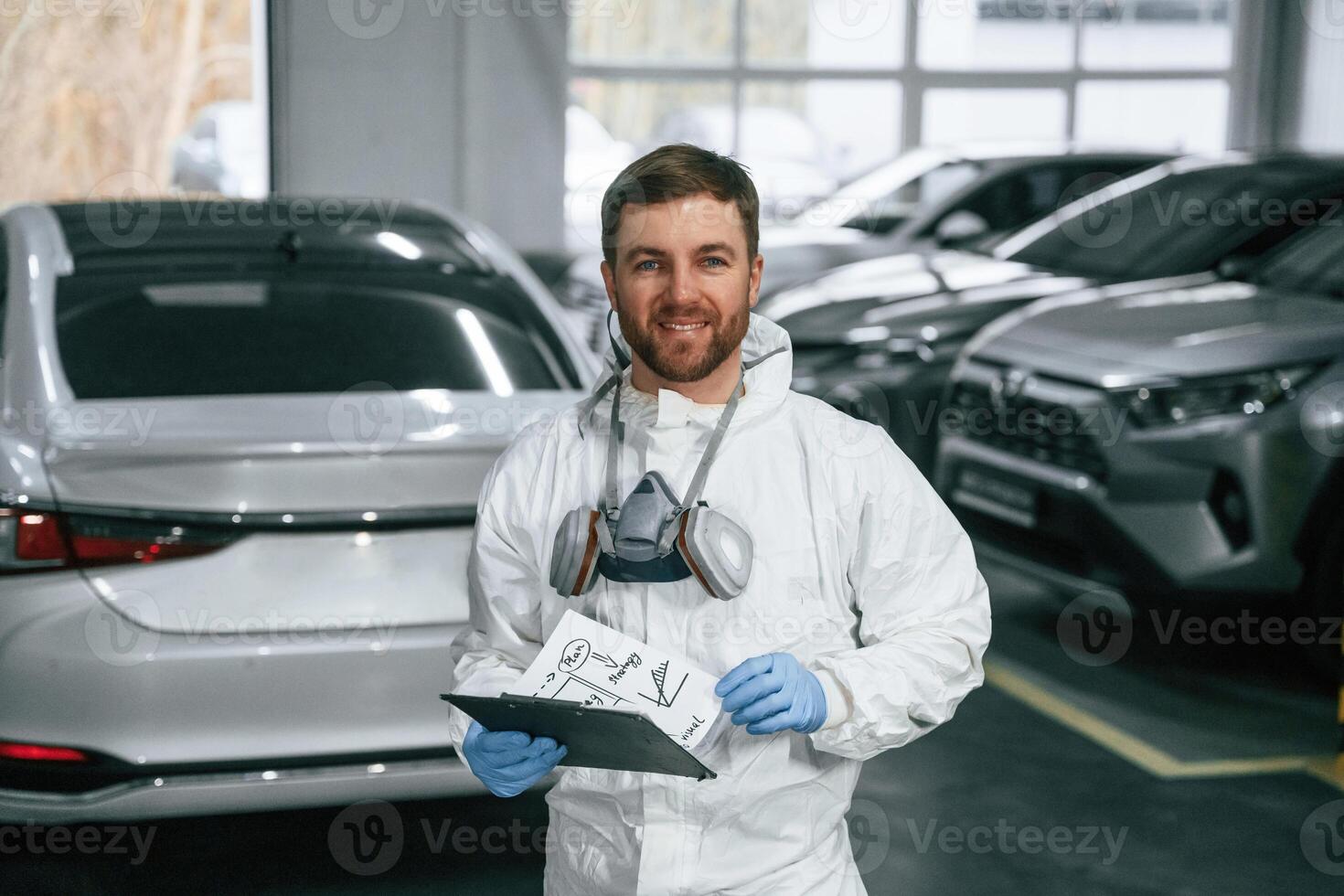 Positive facial, expression. Car painter is standing in the garage with documents in hands photo