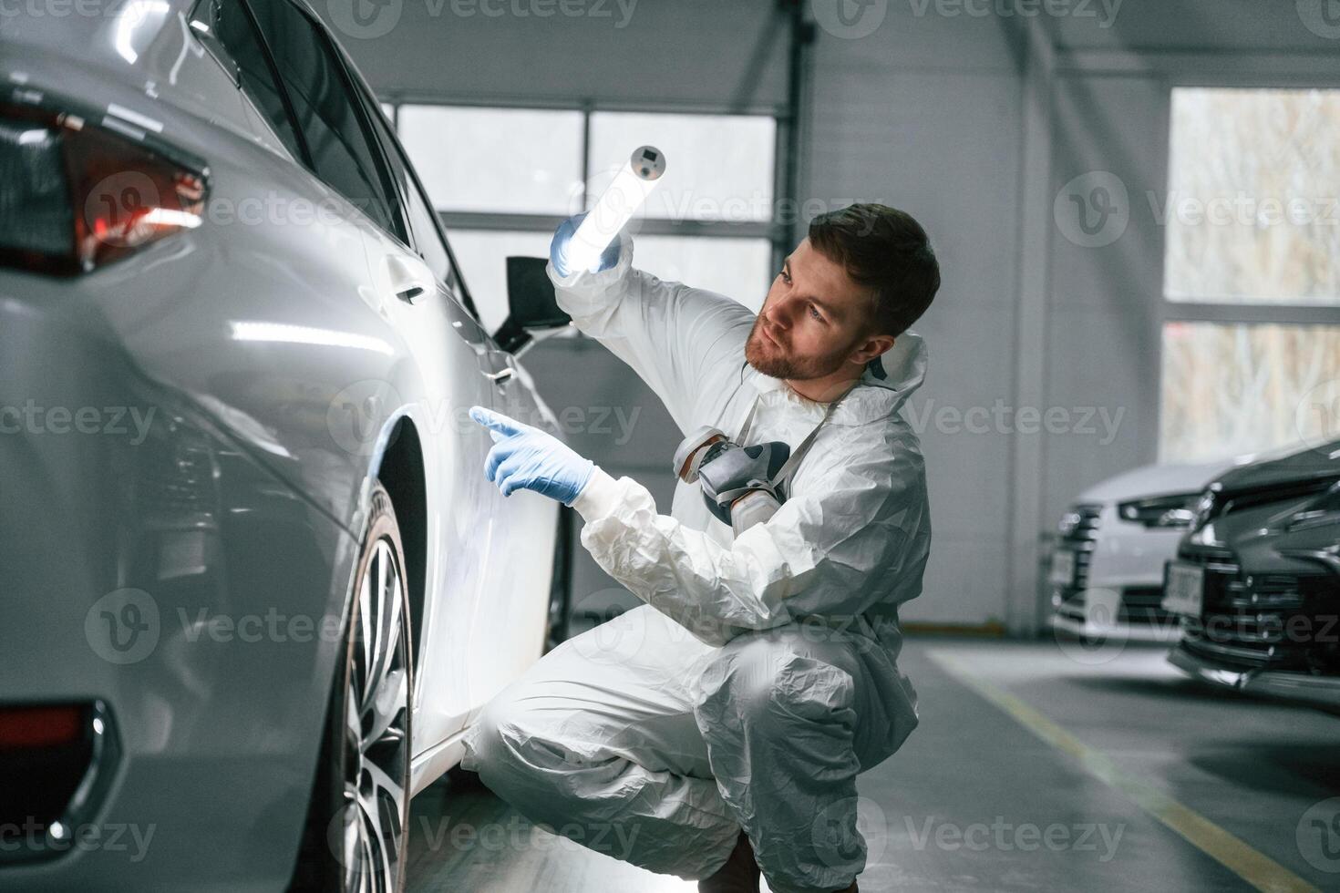 Searching, for imperfections. Garage worker is holding lighting and checking surface of the car photo