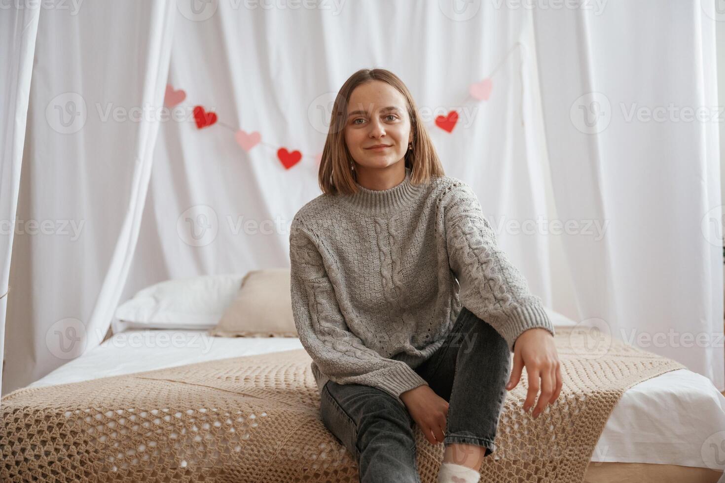 Portrait ,of young woman sitting at home in domestic room against paper hearts decoration behind her photo