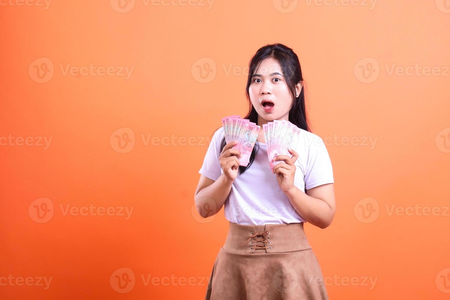 Surprised woman holding two stacks of Indonesian Rupiah notes with an orange background photo