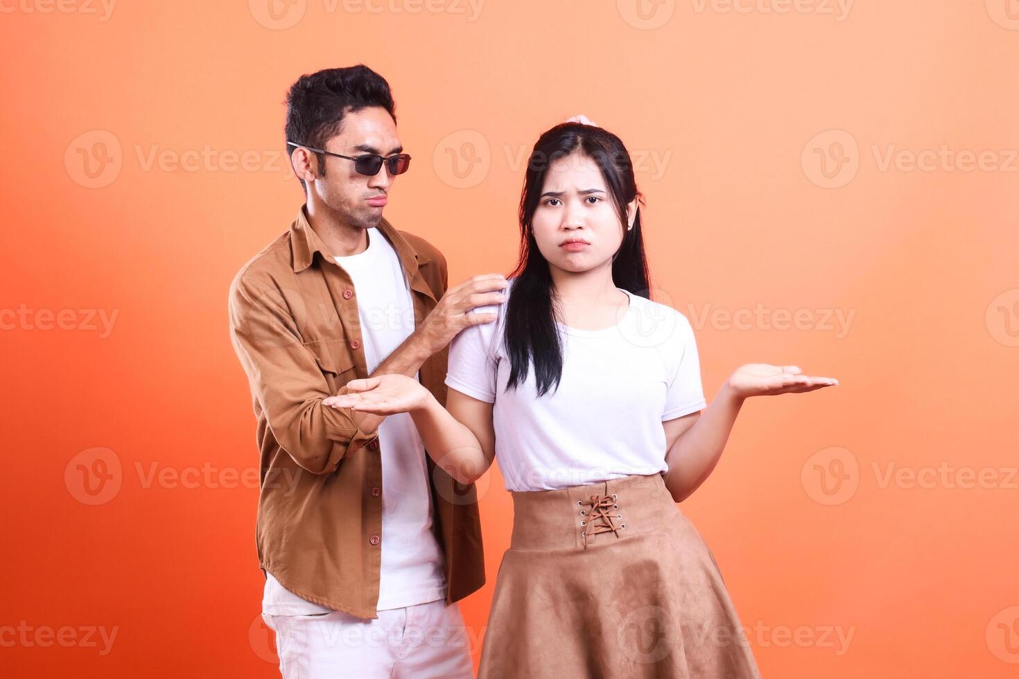 a adult couple of lovers with surprised expressions looking forward where the man is standing and the woman is looking forward romantically. isolated on orange background photo