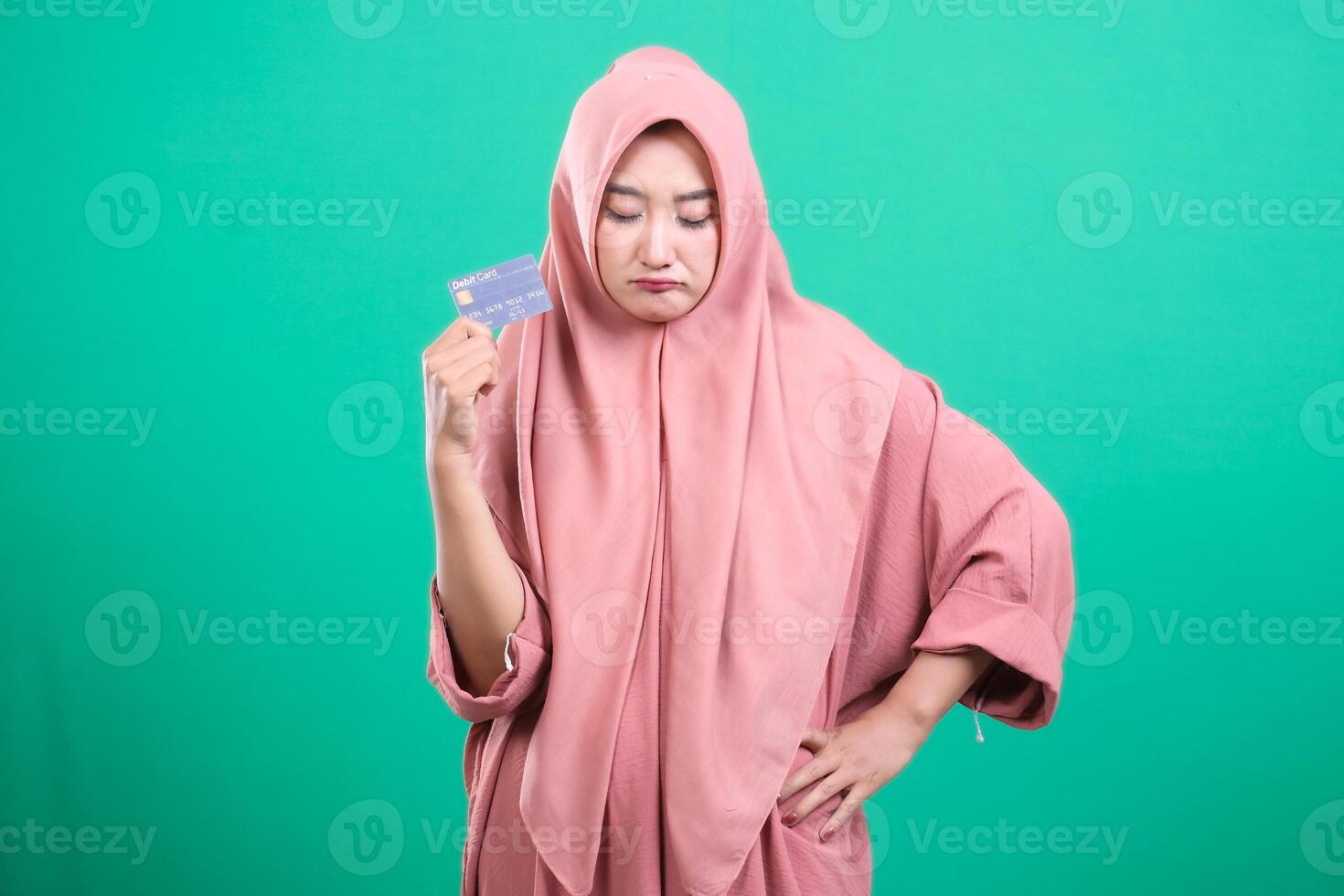 Disappointed muslim woman holding a credit card looking down fee photo