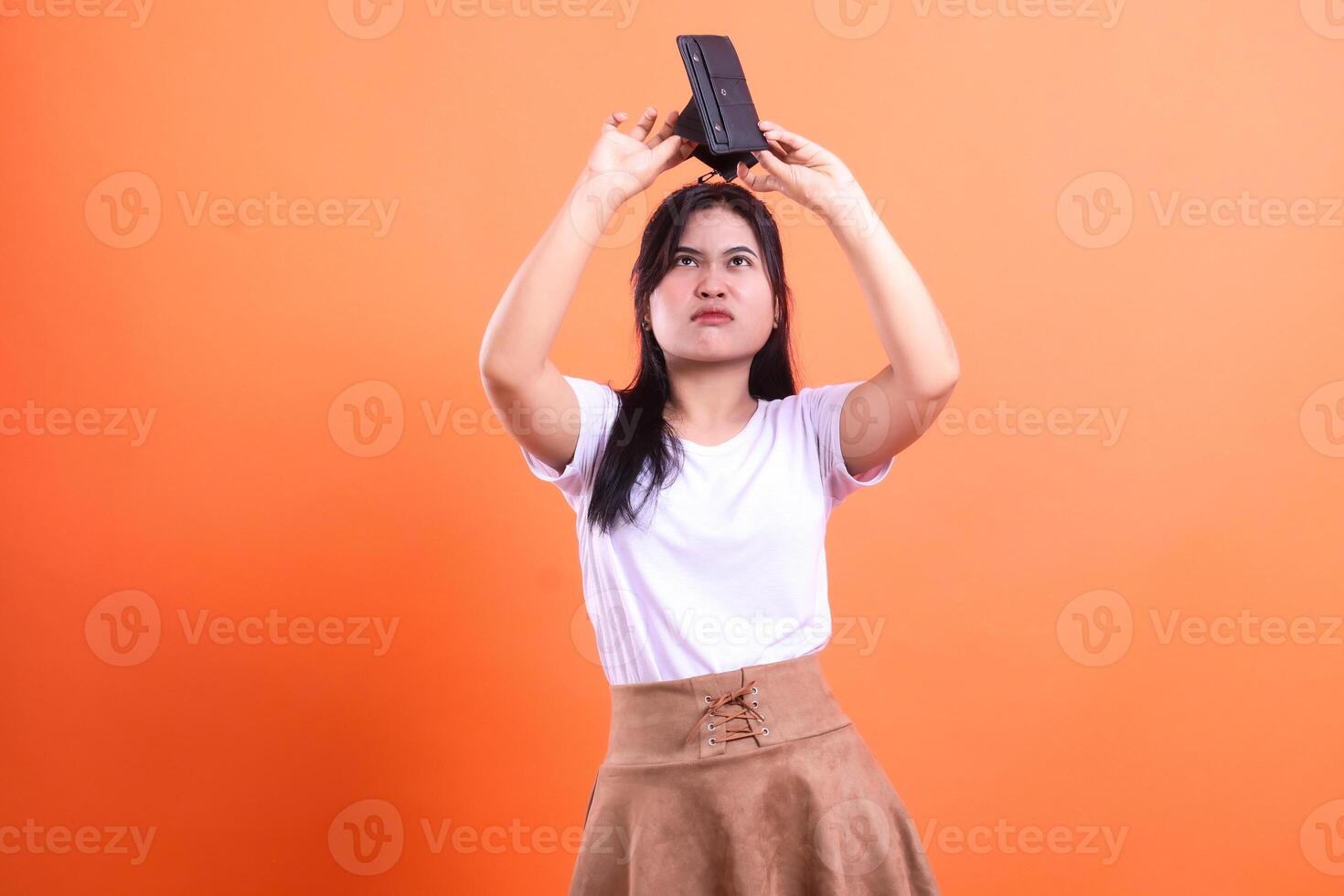 Woman holding a black object over her head against an orange background in studio shot photo