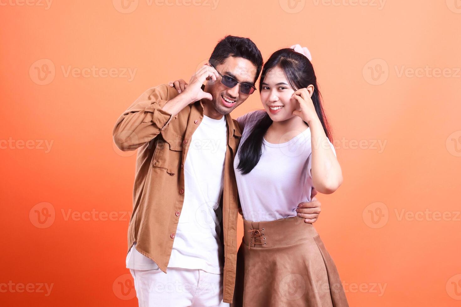 a pair of young lovers happy expression where the man stands and the woman hands sign love facing the camera romantic. isolated on orange background photo