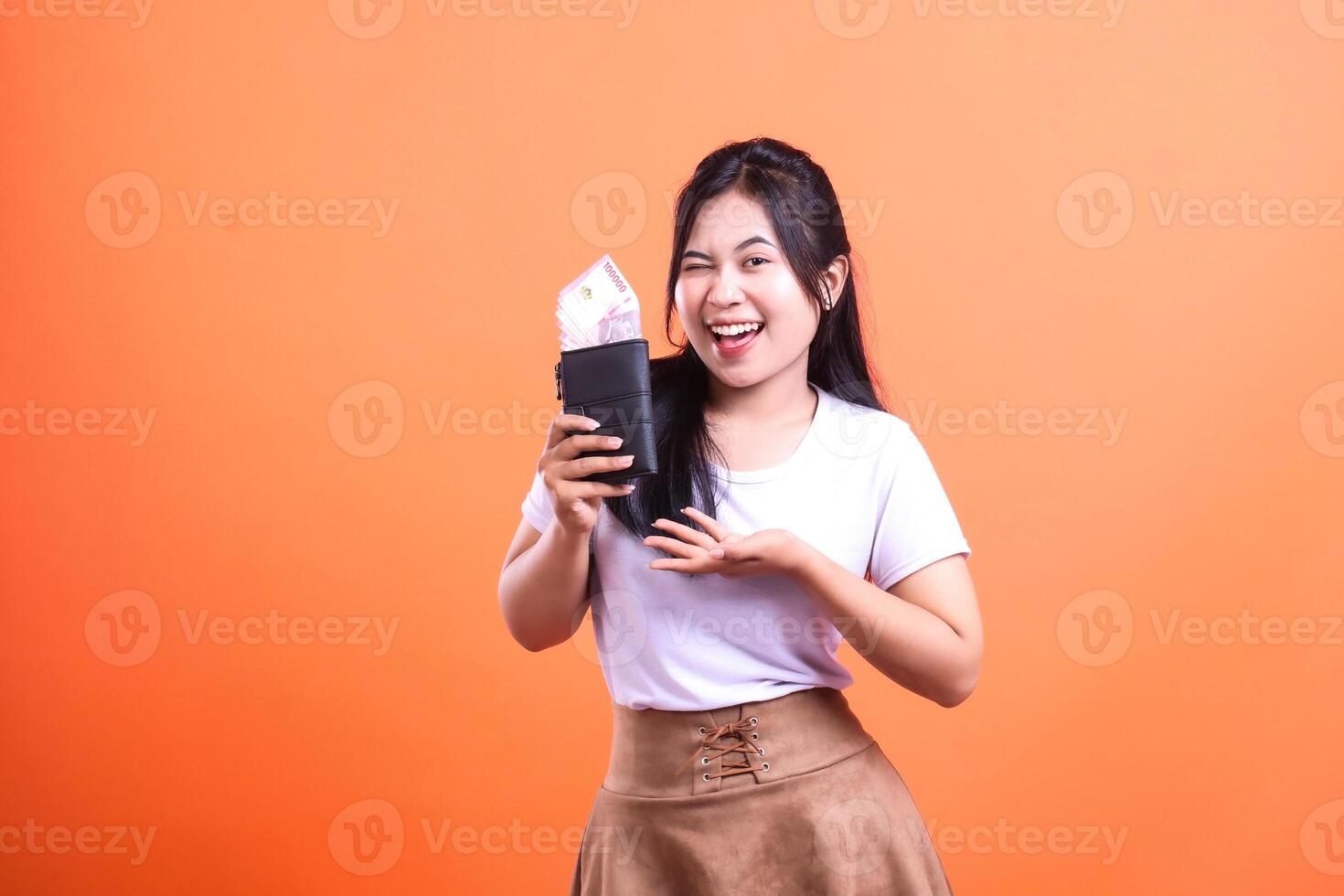 A Smiling Woman Holding a Wallet Full of Money on an Orange Background photo