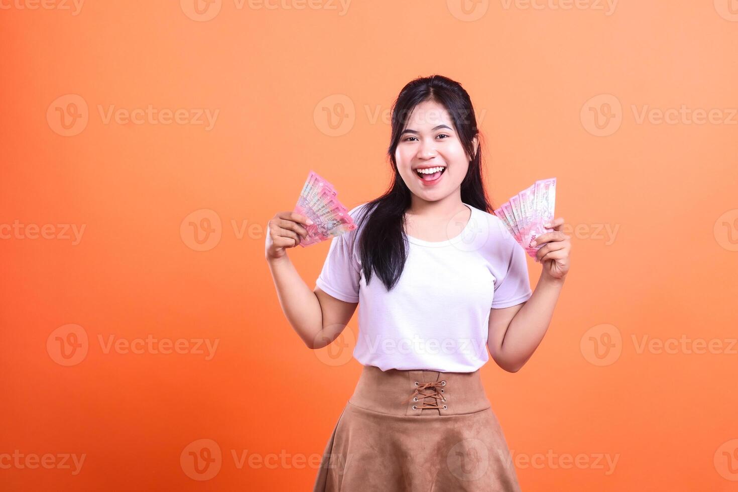 Woman smiling and holding money in both hands on an orange background photo