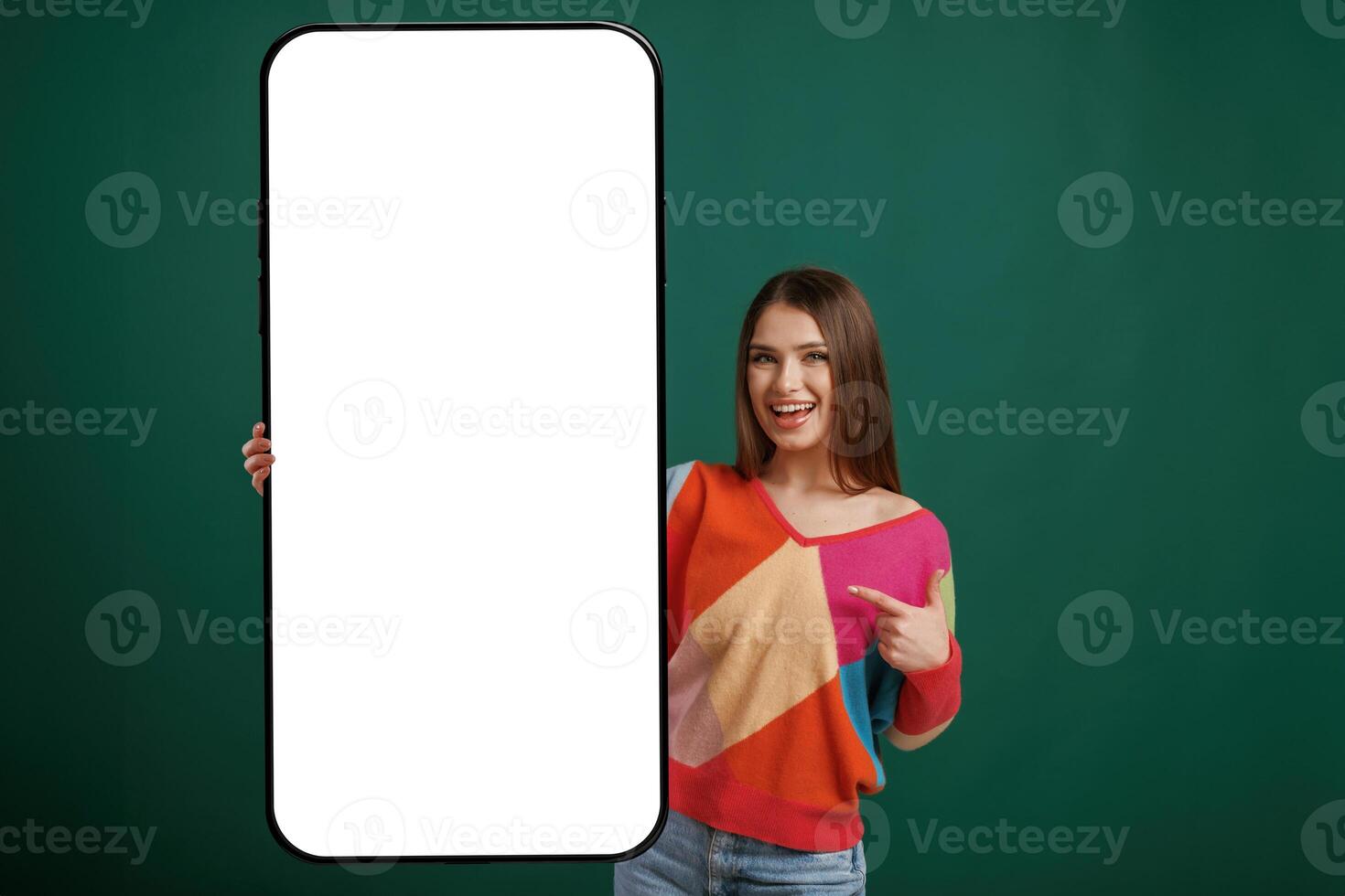 Large smartphone. White ,display ,for text or design. Young woman is standing against green background in the studio photo