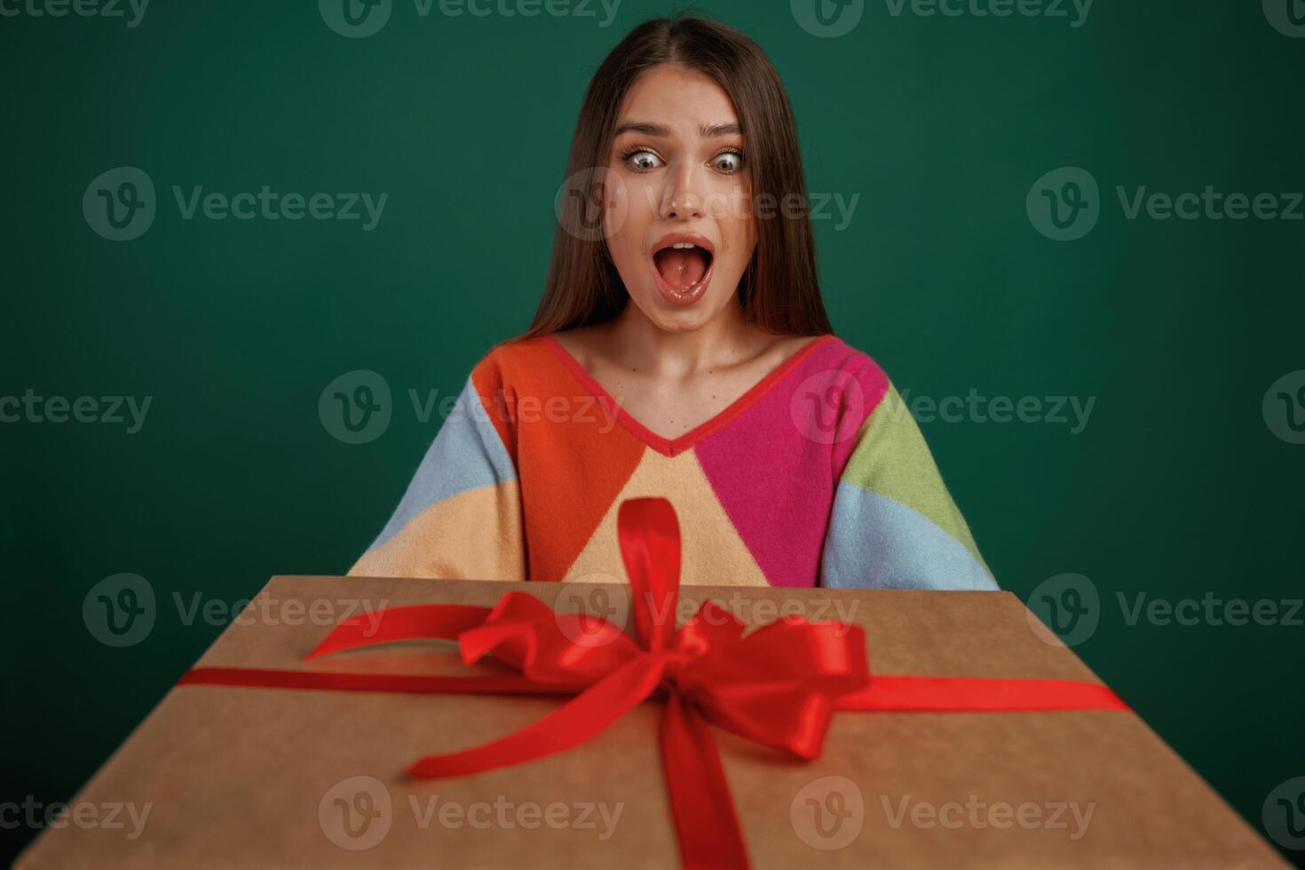 Surprised, holding ,box ,gift box. Young woman is standing against green background in the studio photo