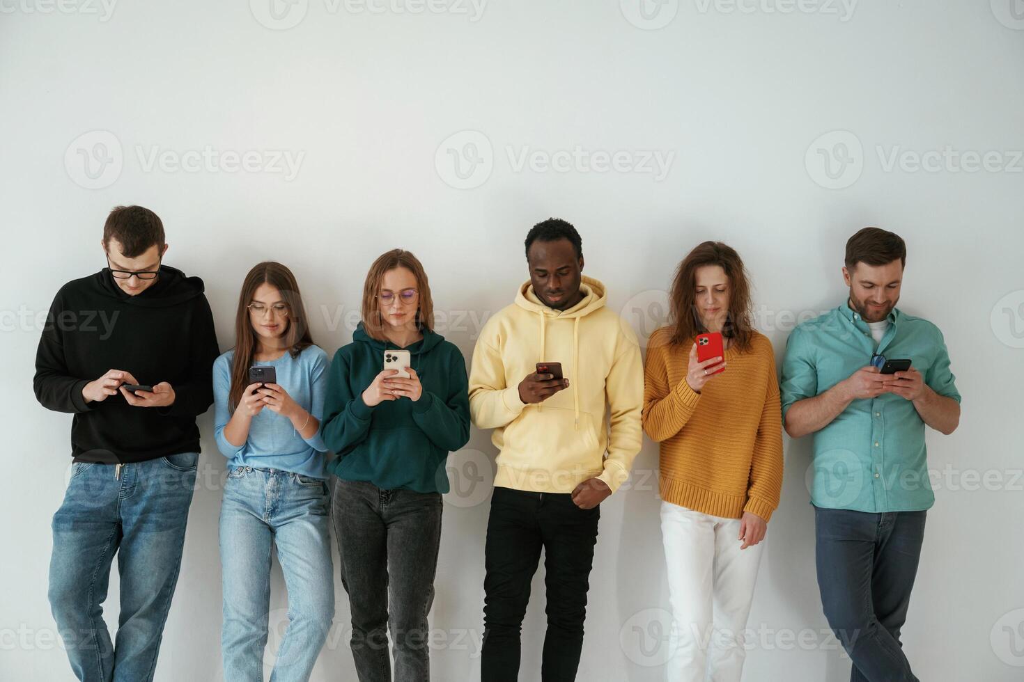 Busy, by using smartphones. Group of young people are standing against white background photo
